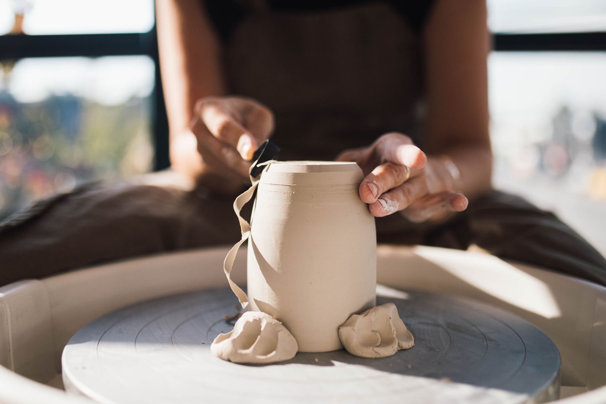 A woman crafting a pottery vase on a spinning wheel creating a white vase.