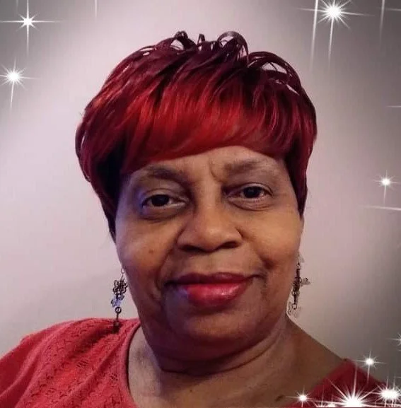 Female police officer in uniform, standing in front of an American flag, smiling, with a blue background.