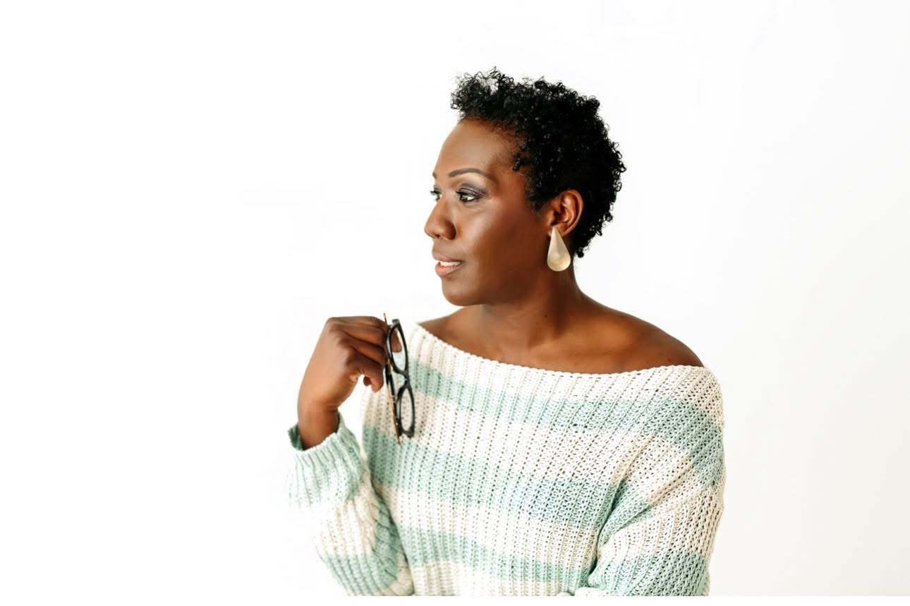 A smiling woman with blonde hair wearing a light blue sweater against a teal background.