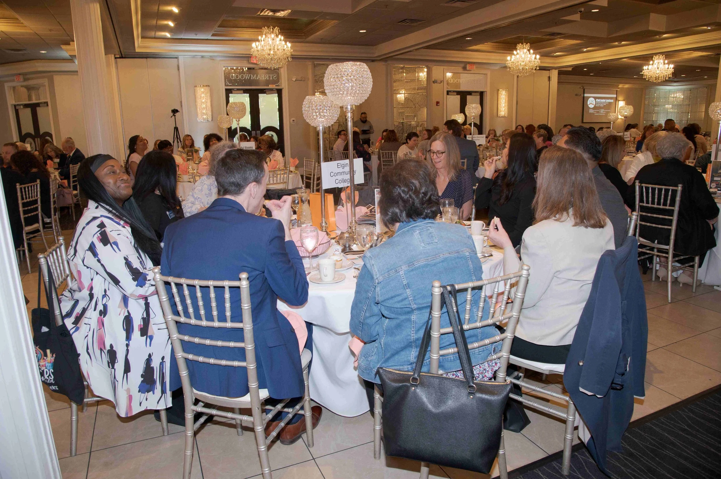 People sitting around tables at a banquet with chandeliers in a large decorated hall.