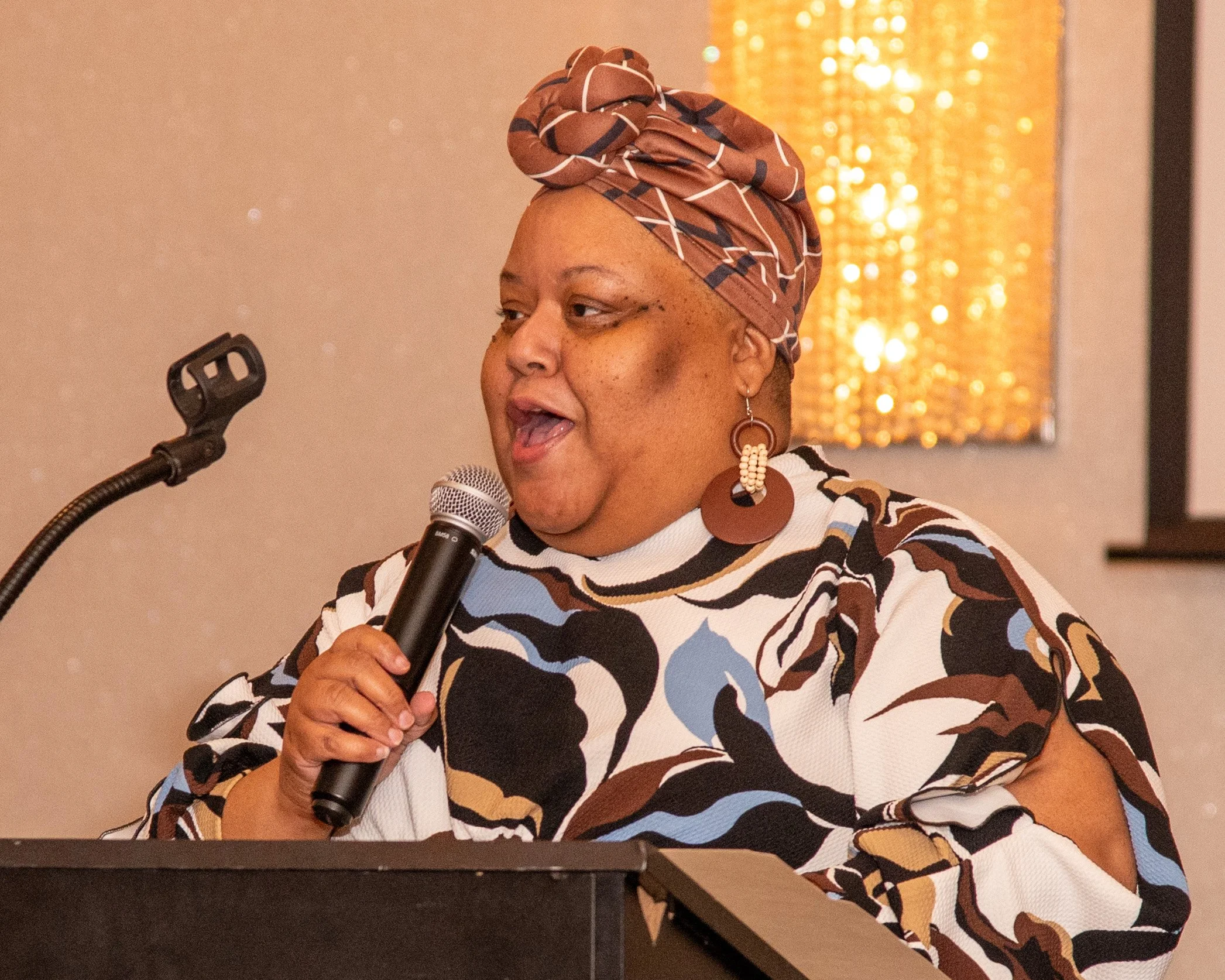 Professional woman with shoulder-length reddish-brown hair, wearing a black robe and white collar, smiling against a gray background.