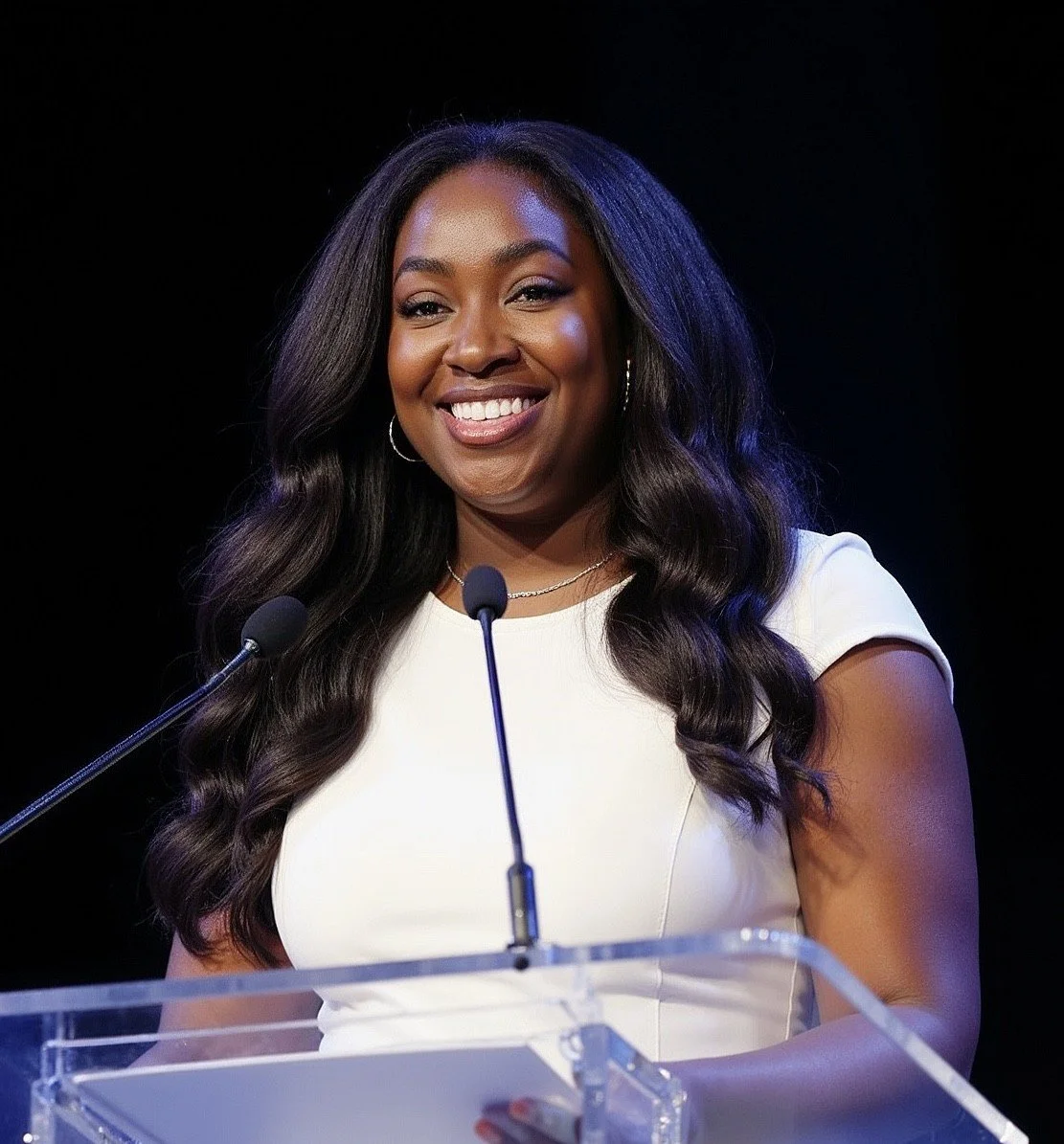 A smiling woman with shoulder-length red hair and blue eyes taking a selfie against an orange background.