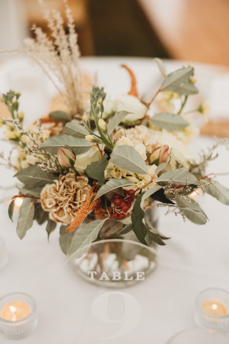 A floral centerpiece with greenery, dried flowers, and berries on a table labeled 'Table 9' with candles around