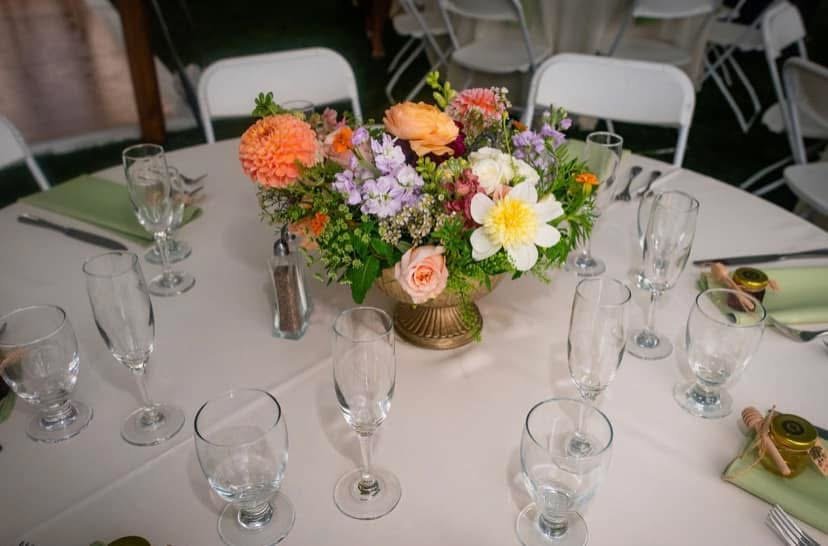 Round table decorated with a flower centerpiece, multiple empty wine glasses, and green napkins with small decorative favors.