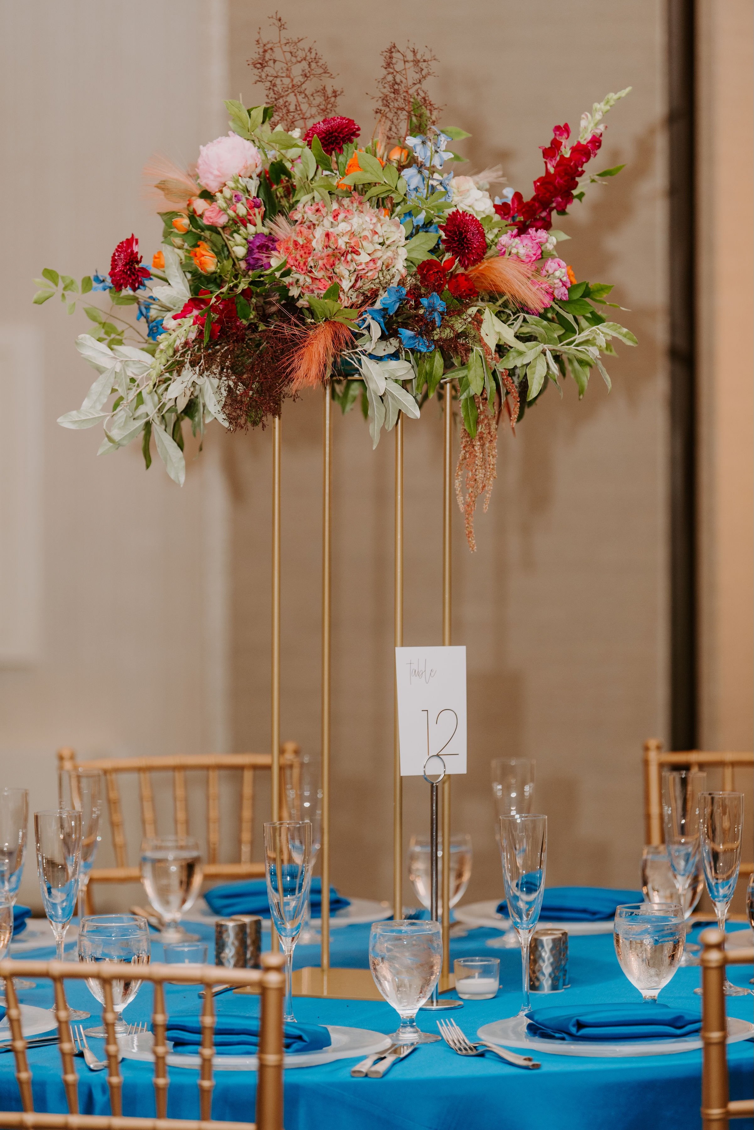 Table centerpiece with a colorful floral arrangement on a tall, gold stand at a formal event.