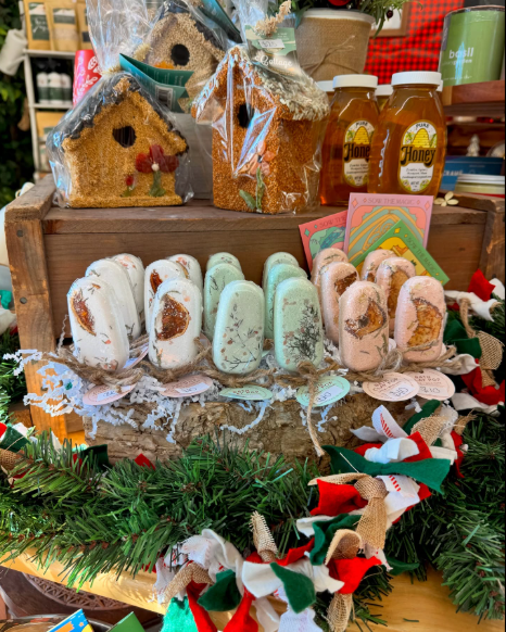 Display of holiday treats including decorated cookies, honey jars, and marshmallow pops on a festive table with greenery and ribbons.