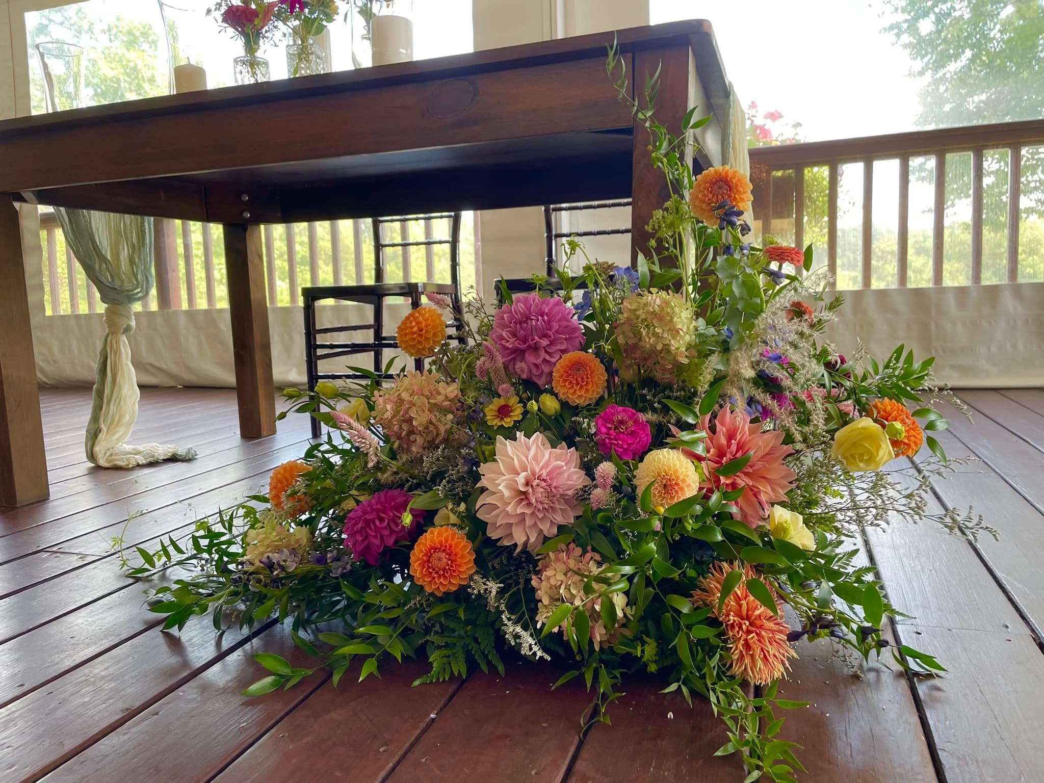 Colorful flower arrangement on a wooden floor near a wooden table with sunlight shining through a window.