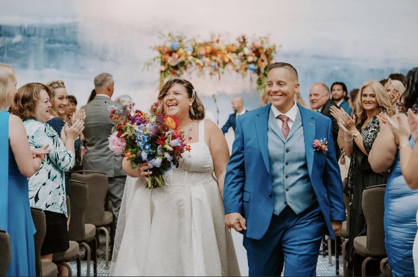 Bride and groom walking down the aisle at their wedding, surrounded by happy guests clapping.