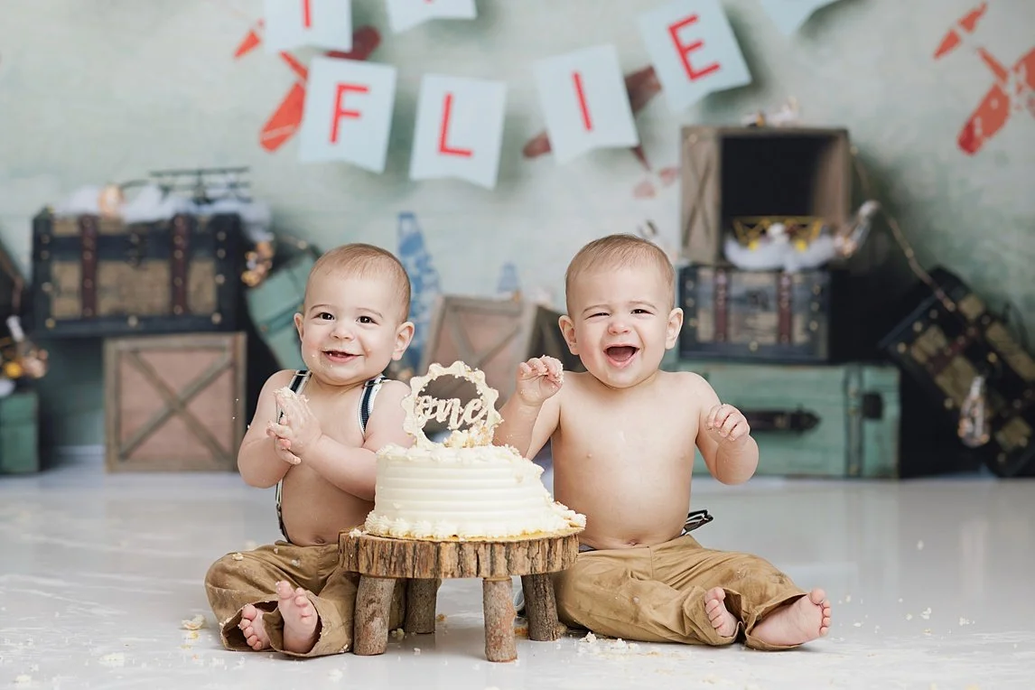 Smiling twin boys sharing their first birthday cake during a vintage airplane-themed cake smash in Southlake, DFW.