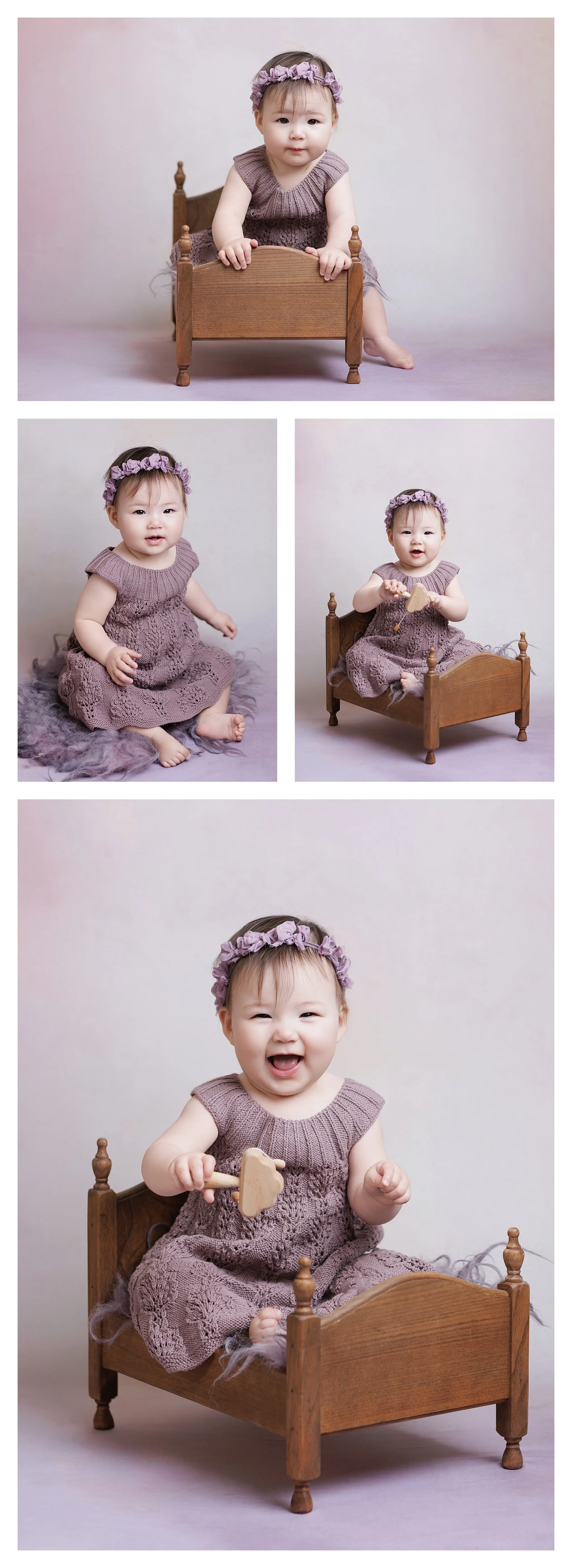 a baby girl in a dusty lavender knit dress and floral headband, sitting on a blanket and a miniature wooden bed, smiling and playing with a wooden toy.