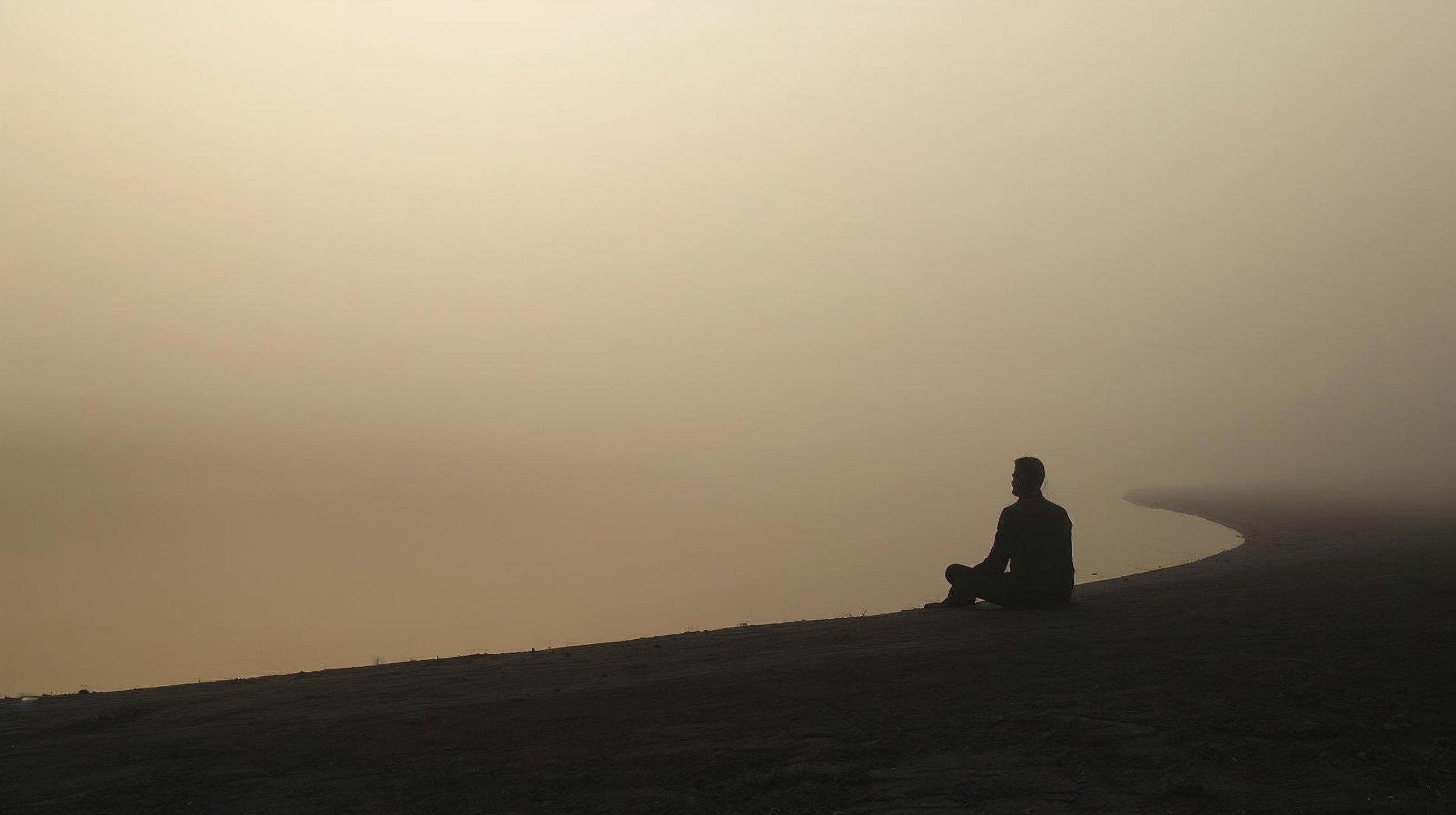 Silhouet van een persoon zittend aan het water in stilte, symbool voor innerlijke leegte en herstel