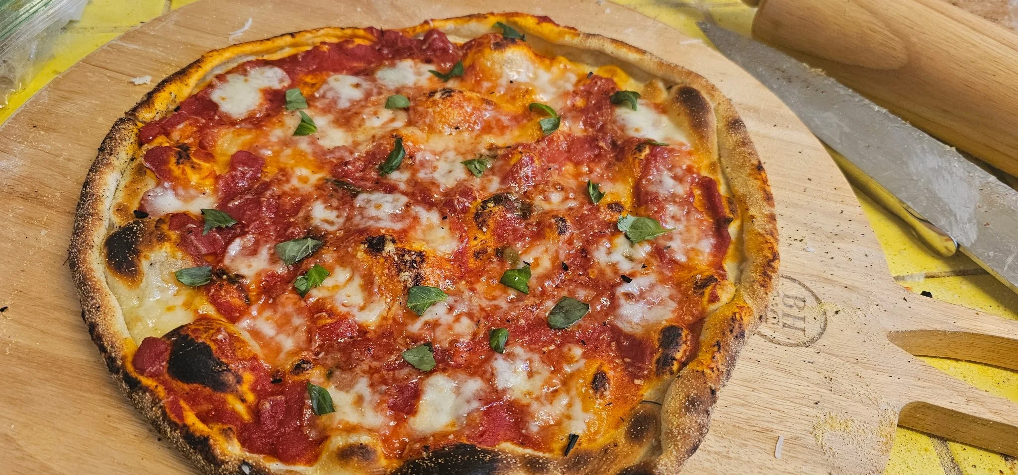 A freshly baked pizza with a slightly burnt crust, topped with tomato sauce, melted cheese, and chopped green herbs on a wooden pizza peel.