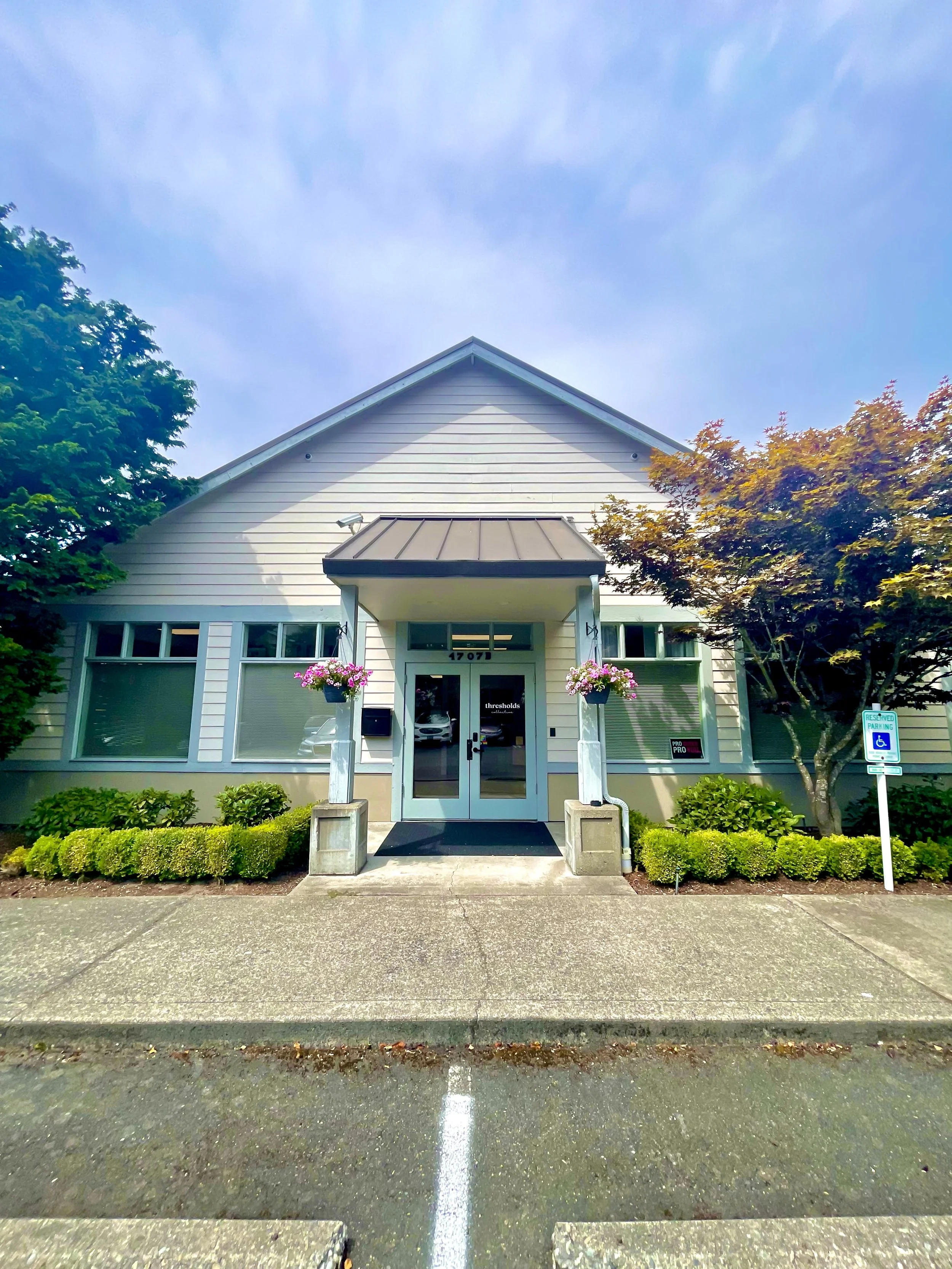 A welcoming front entrance to the pelvic floor & women’s health PT clinic building surrounded by trees, bushes and flower baskets. The large doorway is easy for people with back pain, pelvic pain, pregnant or postpartum moms to enter the building.