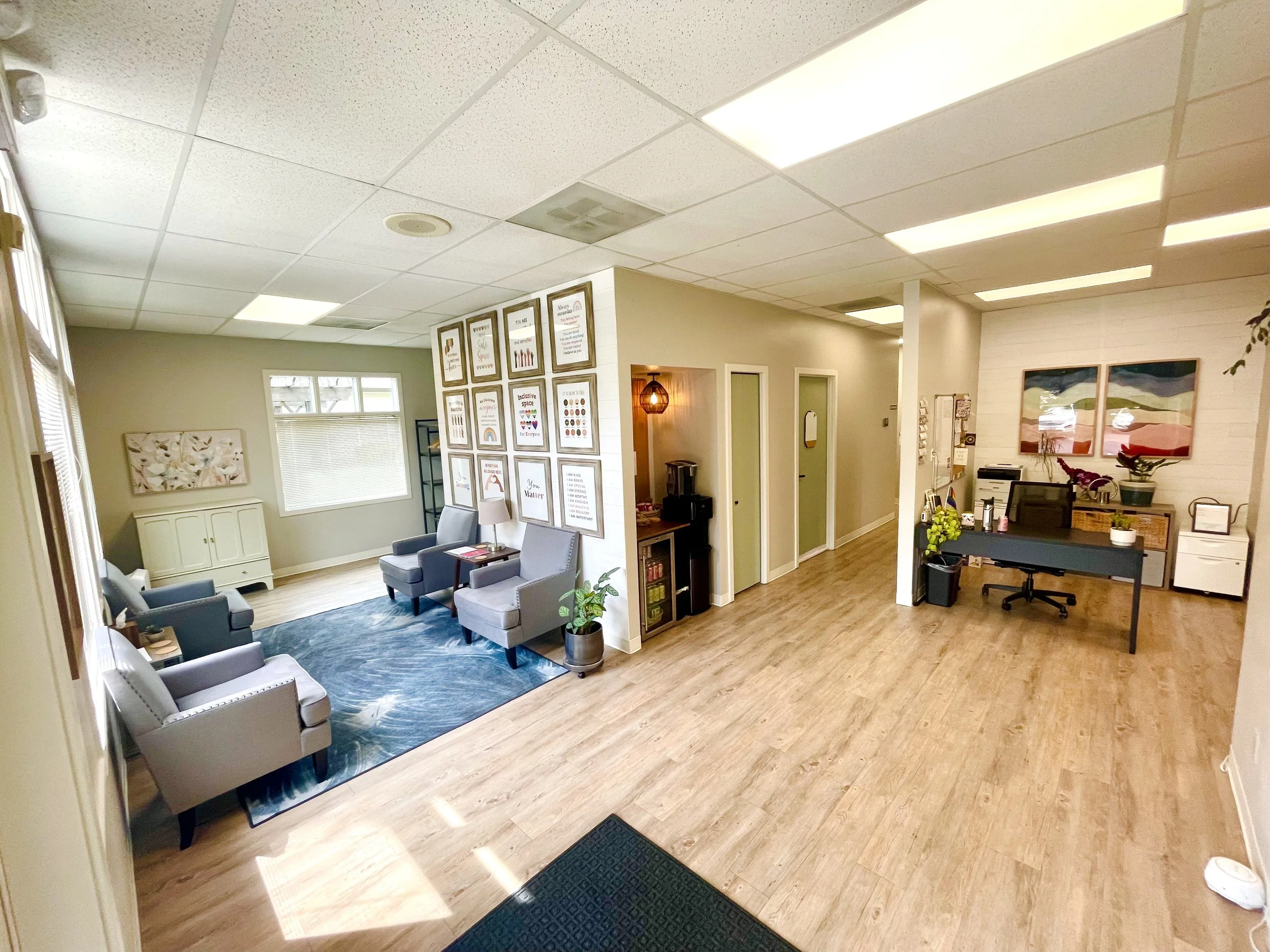 Welcoming, spacious pelvic floor PT clinic reception and waiting area with comfy, wide chairs, snacks and drink station. Inclusive, trauma-informed, anti-racist, LGBTQ celebrating artwork is on the wall.