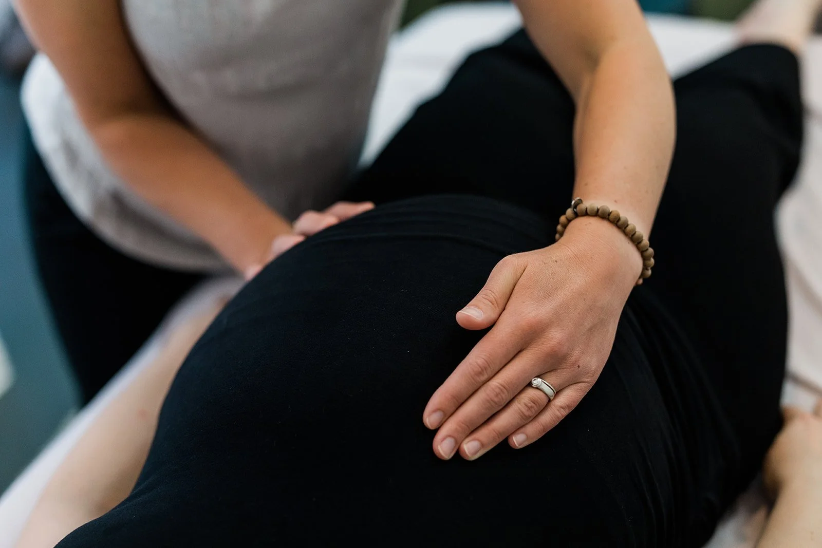 Close-up of a pregnant woman receiving visceral mobilization and holistic pelvic care for birth preparation, with a focus on the hands gently touching her belly, wearing a female anatomy ring and protective bracelet.