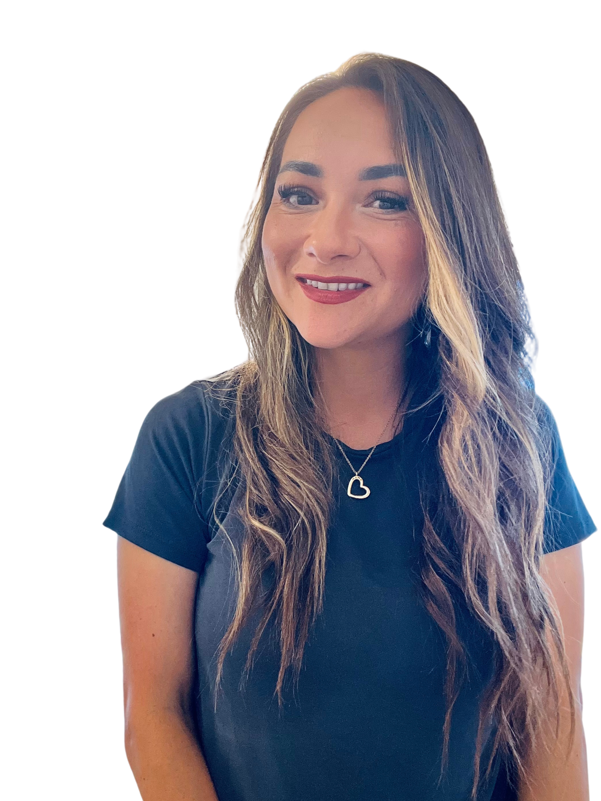 A woman with long, wavy hair smiling, wearing a black t-shirt and a heart-shaped pendant necklace.
