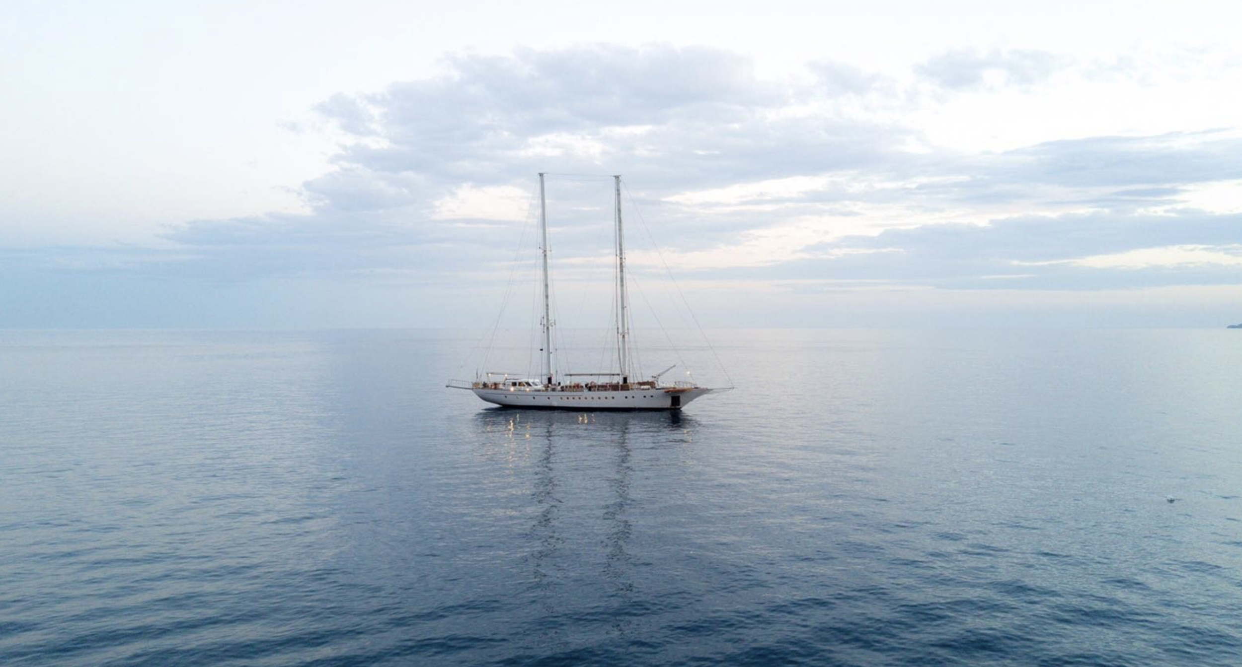 A large sailboat on a calm ocean with a cloudy sky above.