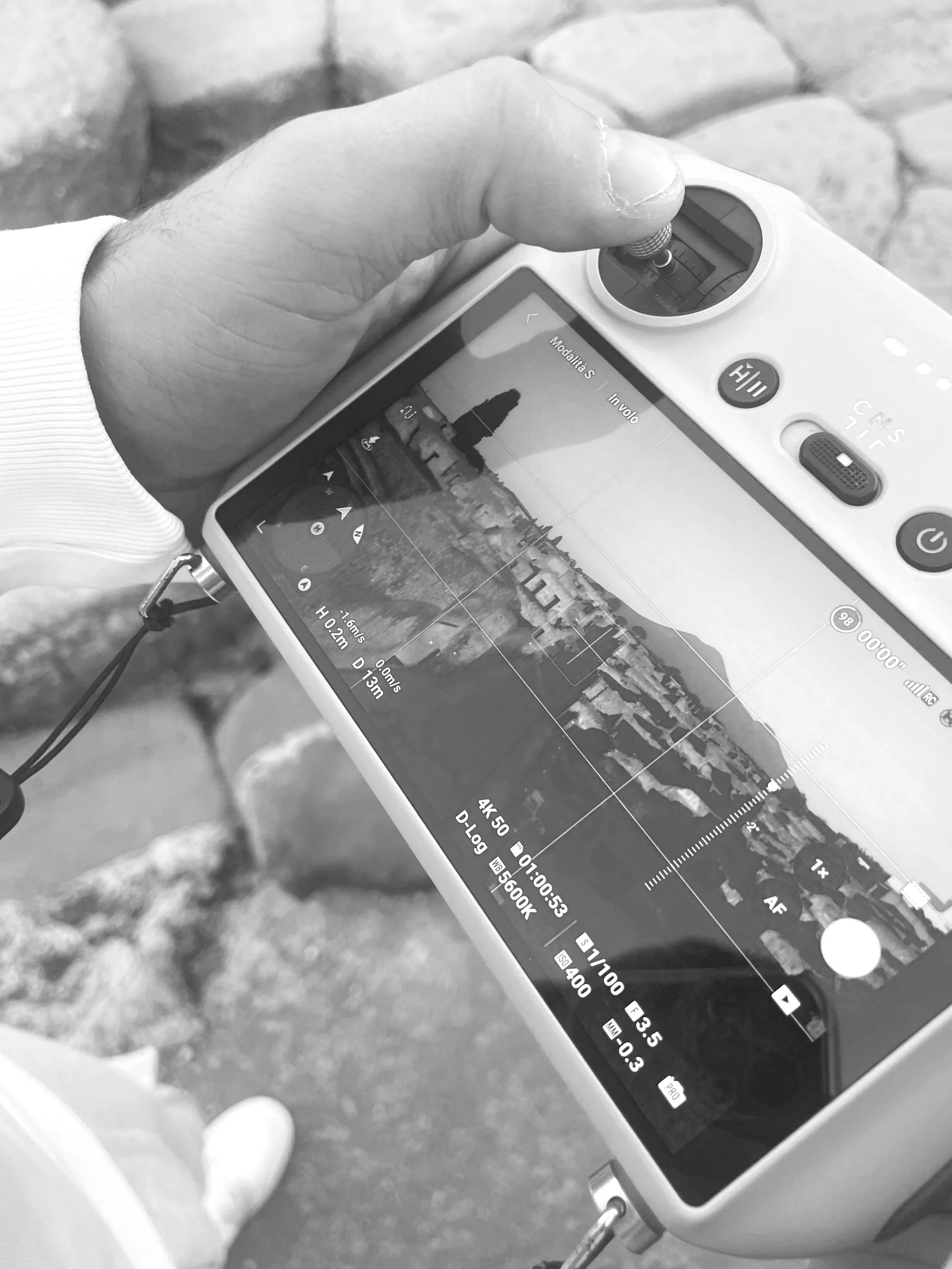 Close-up of a person holding a drone controller with a drone camera view on the screen, capturing a cityscape and river scene.