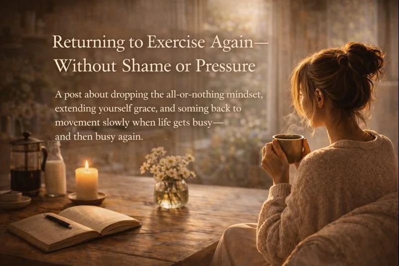 A woman with her hair in a messy bun sitting at a wooden table, holding a mug, with a lit candle, a small bouquet of flowers, an open notebook, and a French press on the table, in a cozy setting.