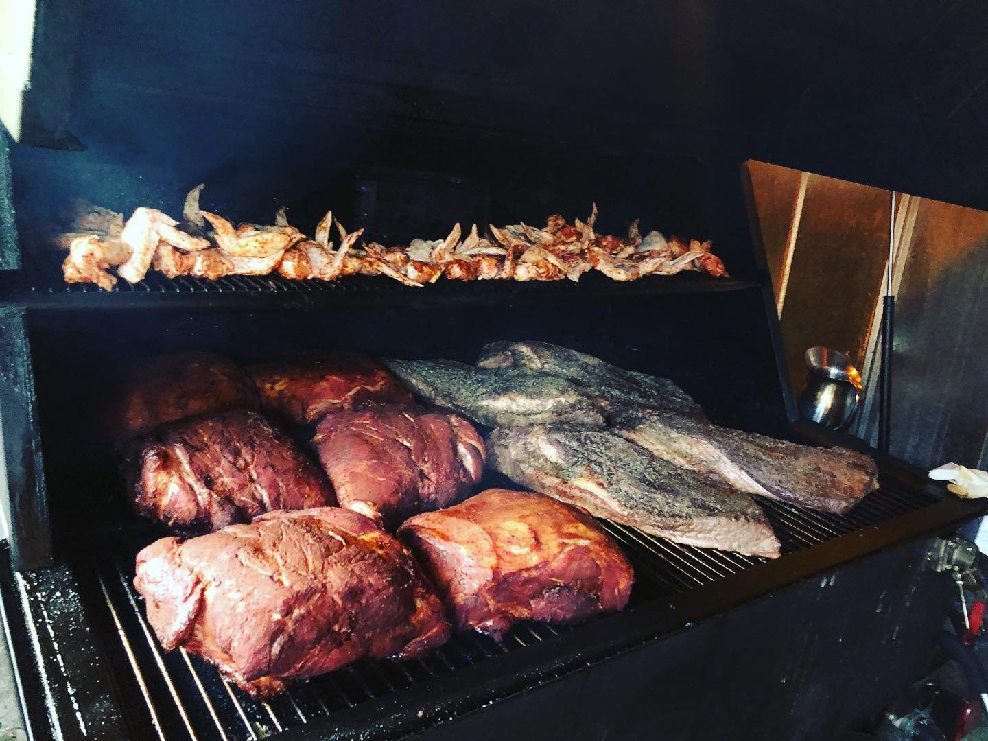 Brisket, pork, and wings, cooking on a smoker.