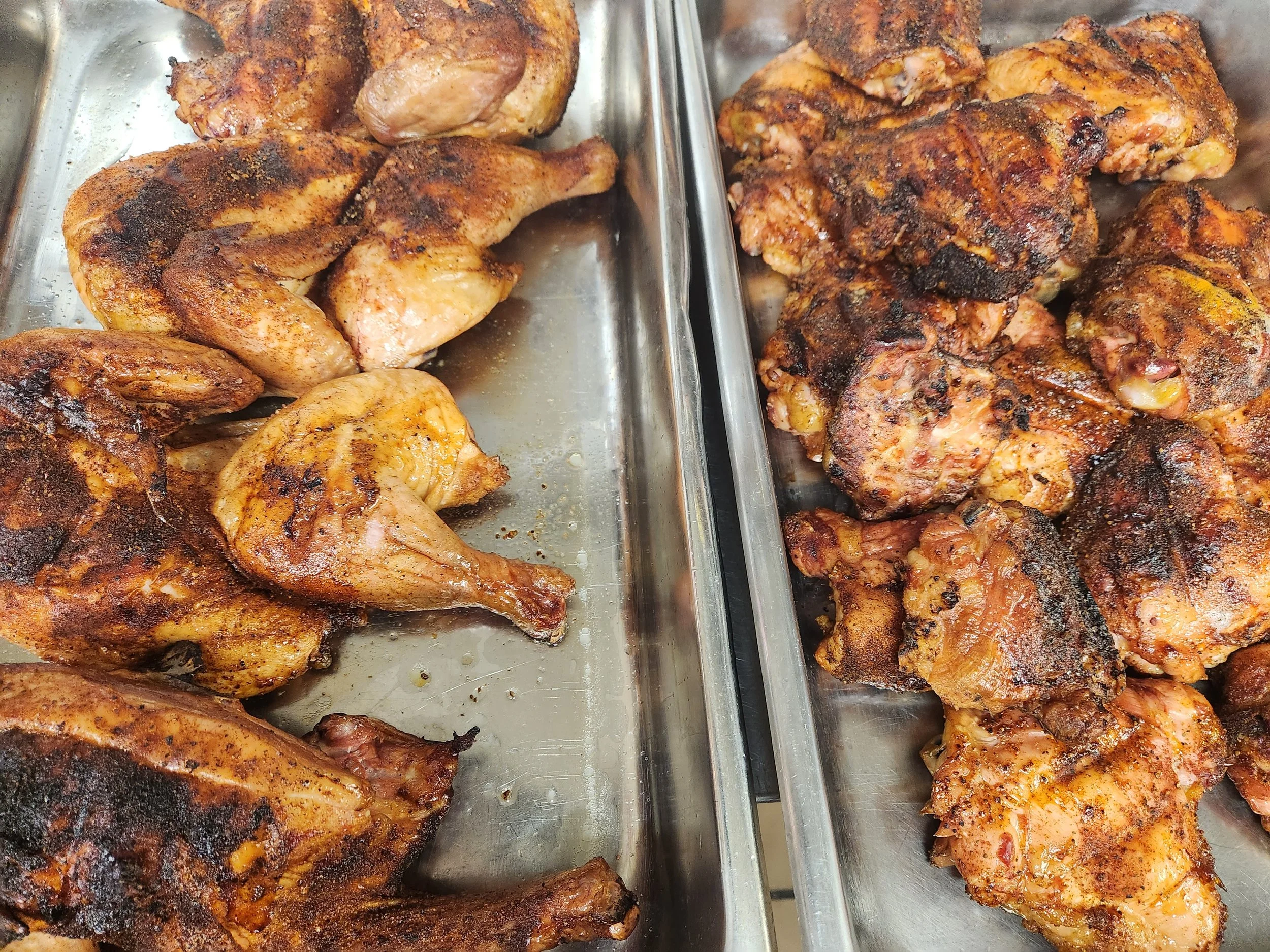 Tray of cooked grilled chicken wings, some with a dark spice rub and charred parts.
