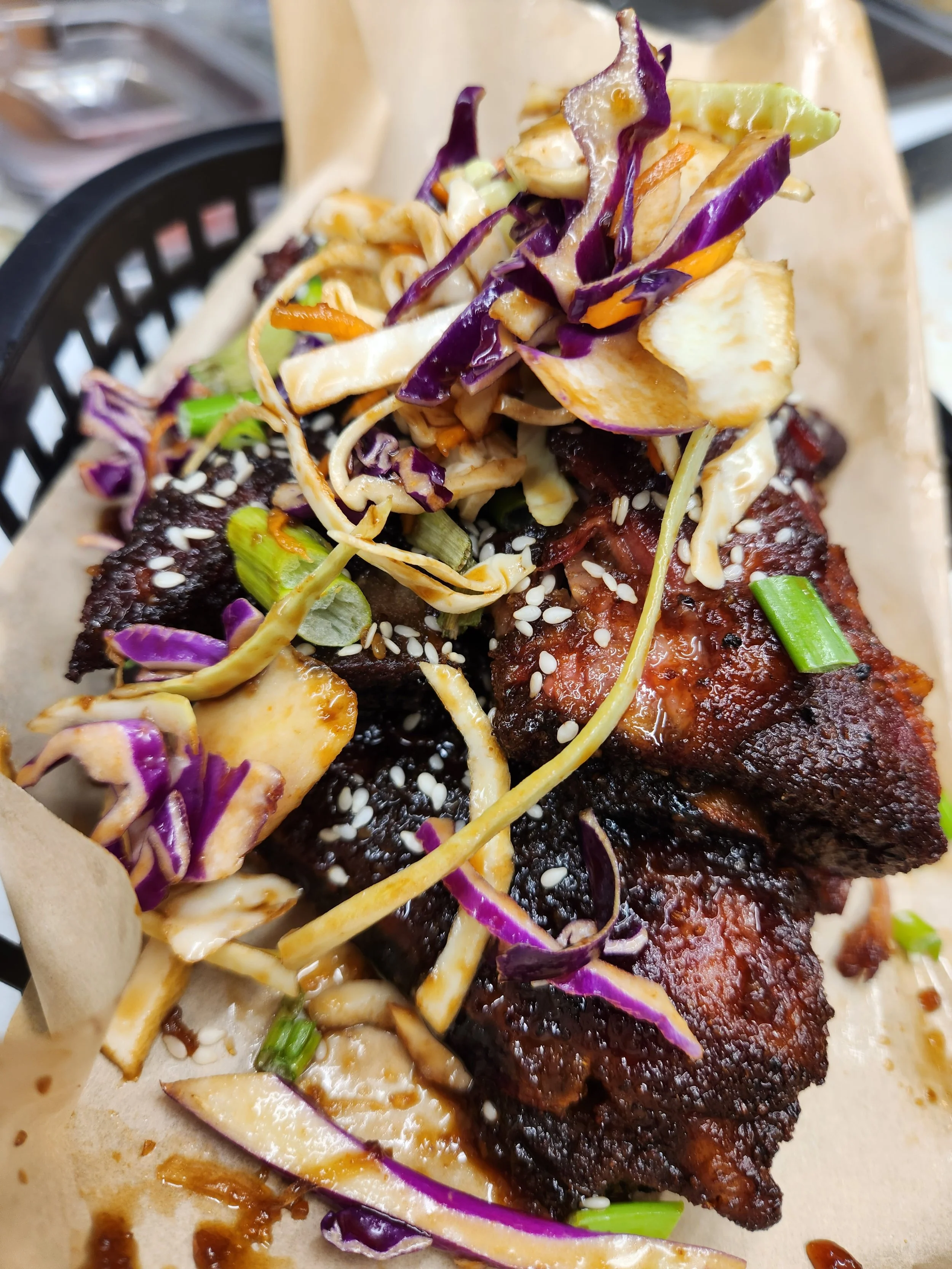 Close-up of Korean-style barbecue ribs topped with shredded cabbage and sesame seeds on a piece of parchment paper.