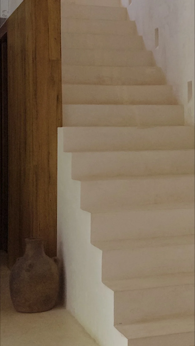 White staircase with beige steps next to a white wall, brown wooden wall on the left, and a brown vase on the floor.