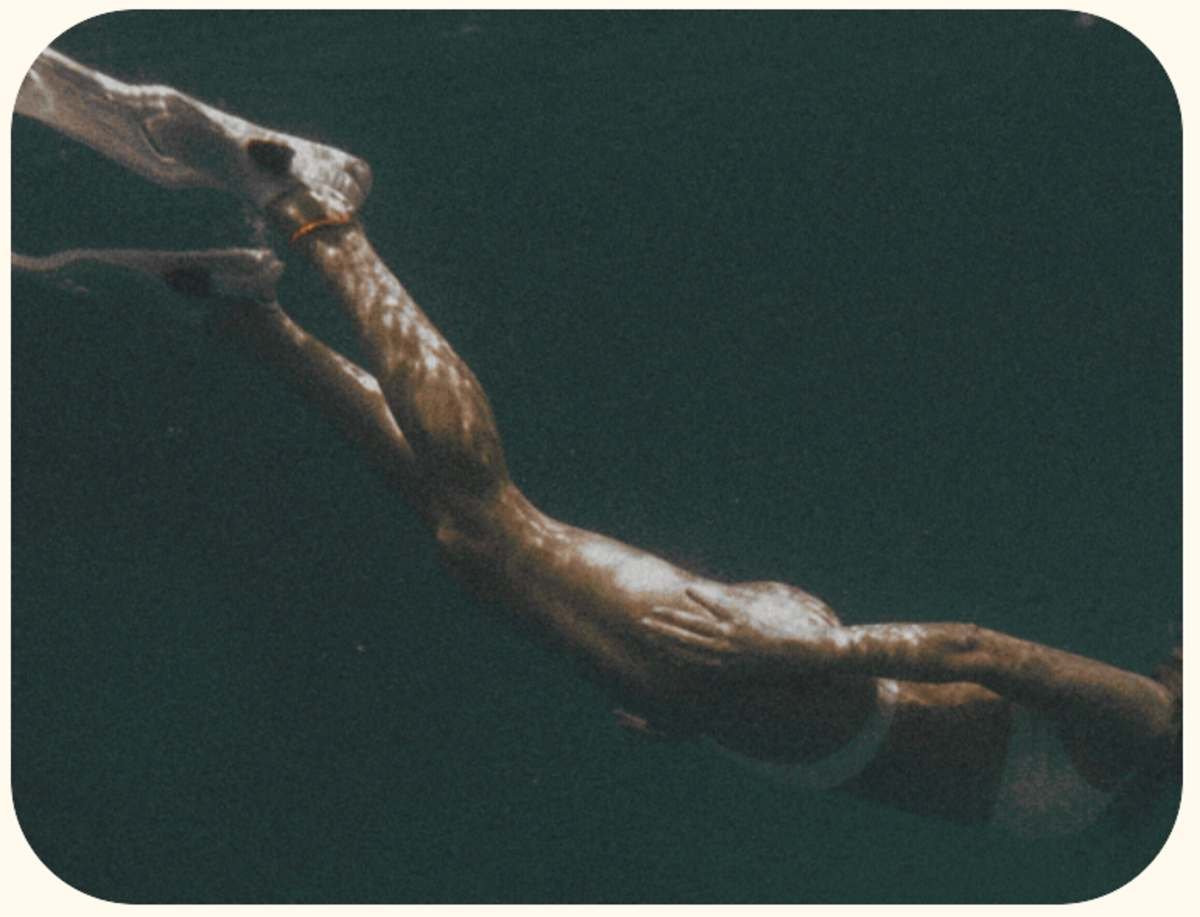 Close-up of a bronze sculpture of two hands reaching for each other against a dark background.