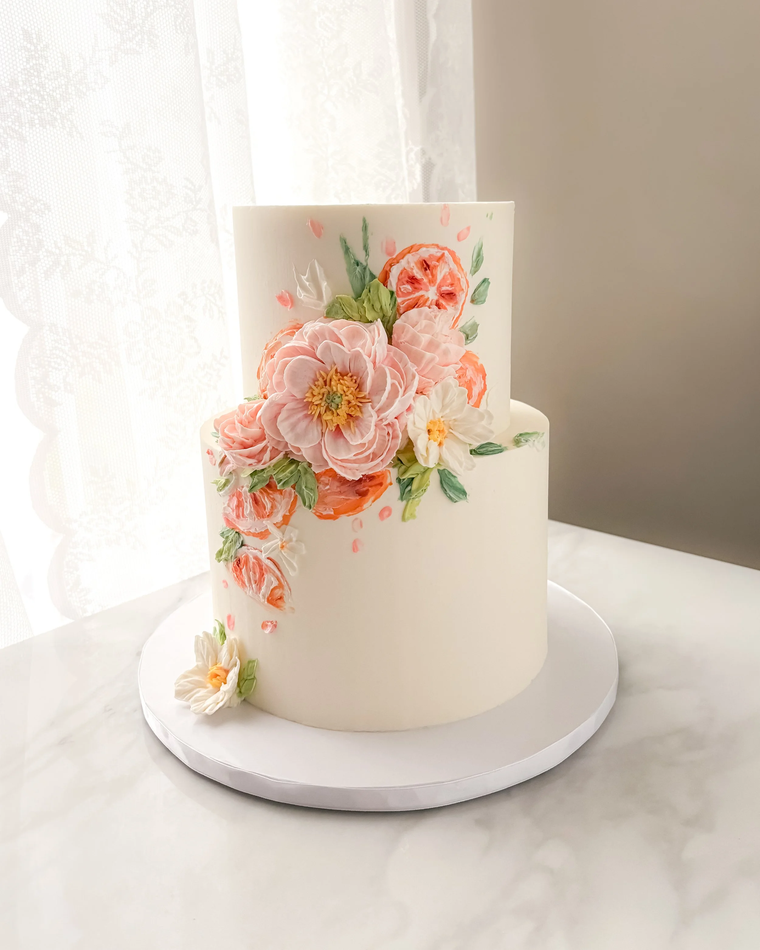 Two-tiered white cake with floral and citrus design in pink and orange