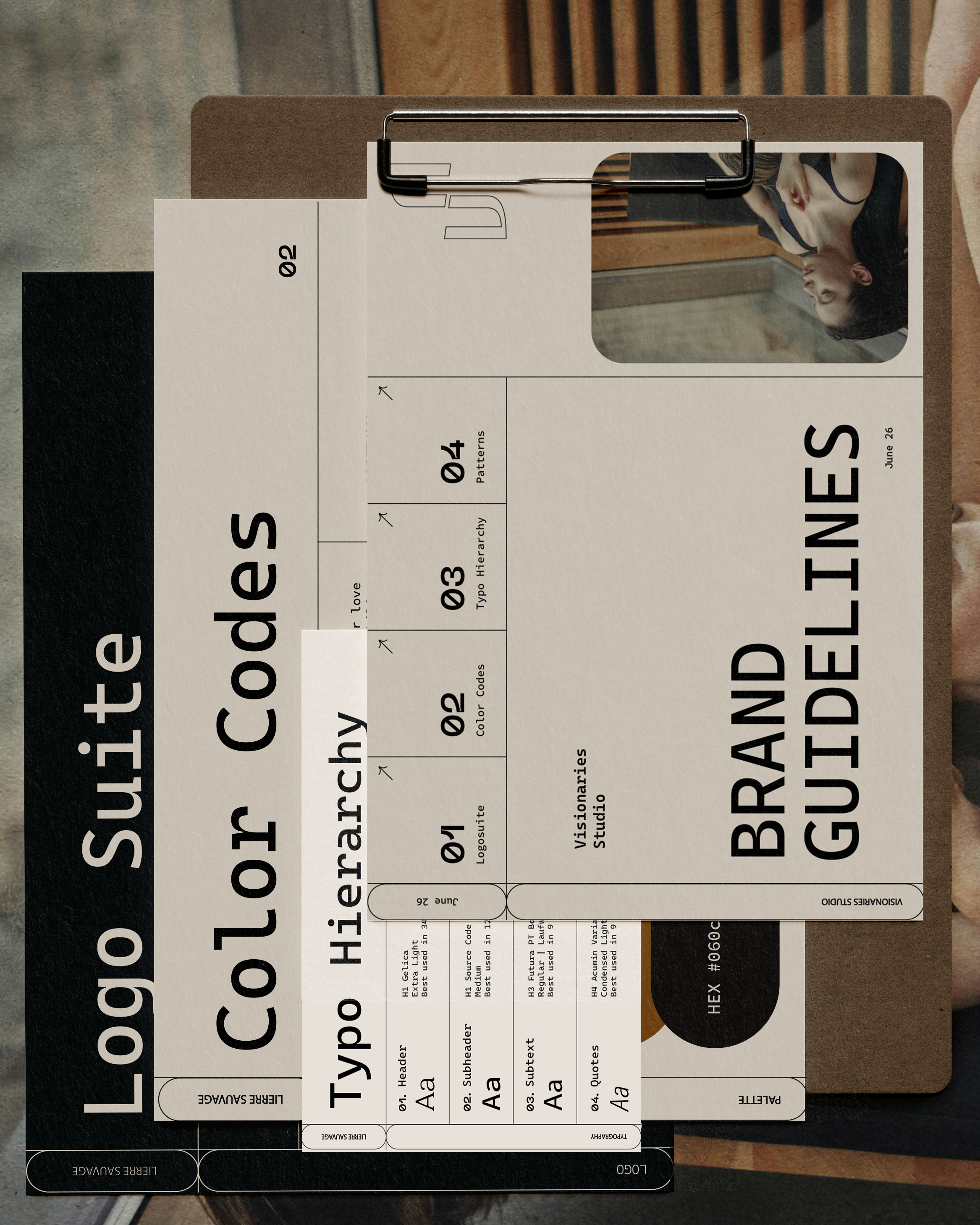 Ein Blick auf eine große Papierbroschüre mit verschiedenen Design- und Typografie-Folien, die auf einem Holztisch liegt, mit einem schwarzen Zeichenblock und einem Metallclip oben.