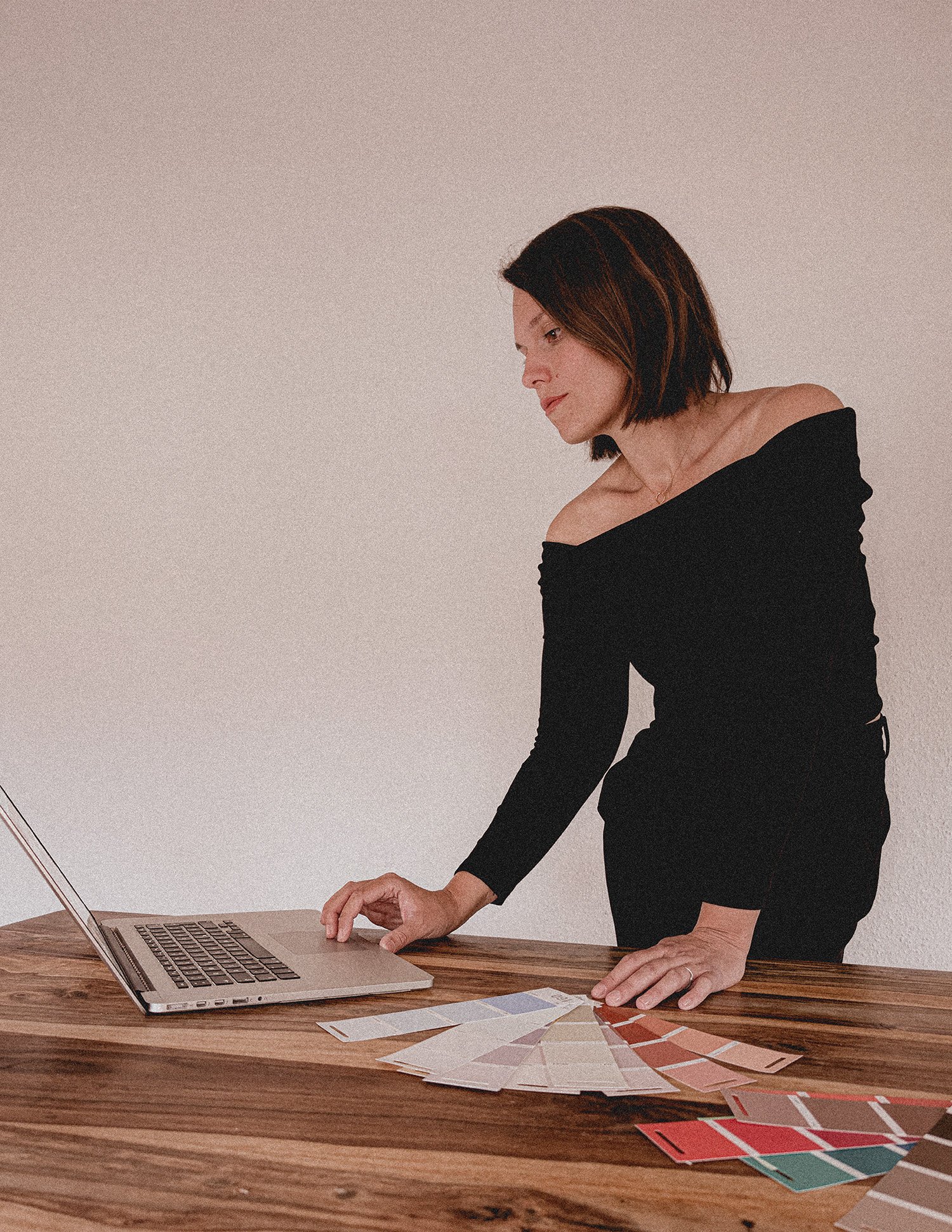 Frau arbeitet an einem Laptop an einem Tisch mit Farbmustern und Farbkarten.