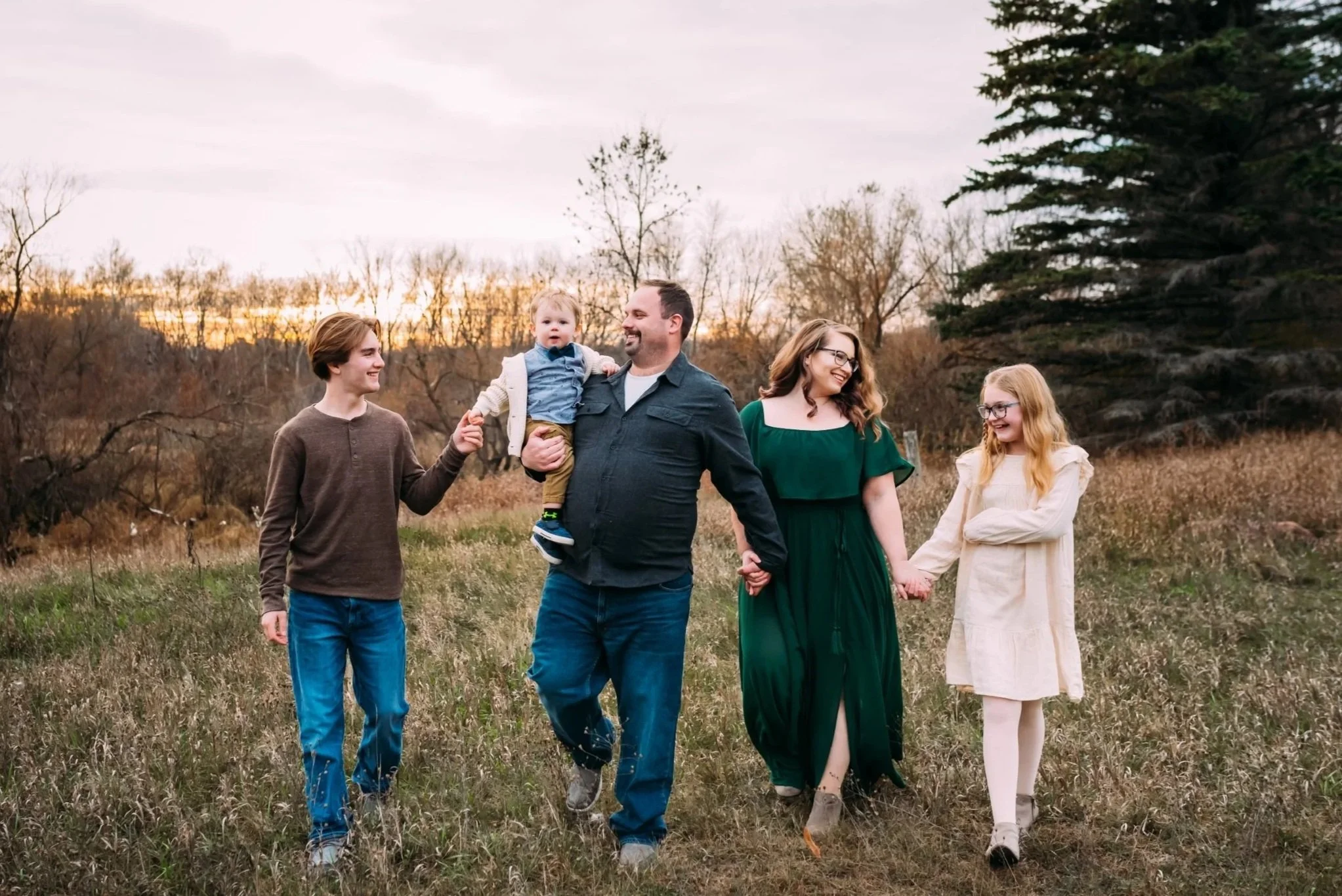 Wausau Photographer captures family photos with Family walking hand in hand happily laughing together in Wausau Wisconsin field