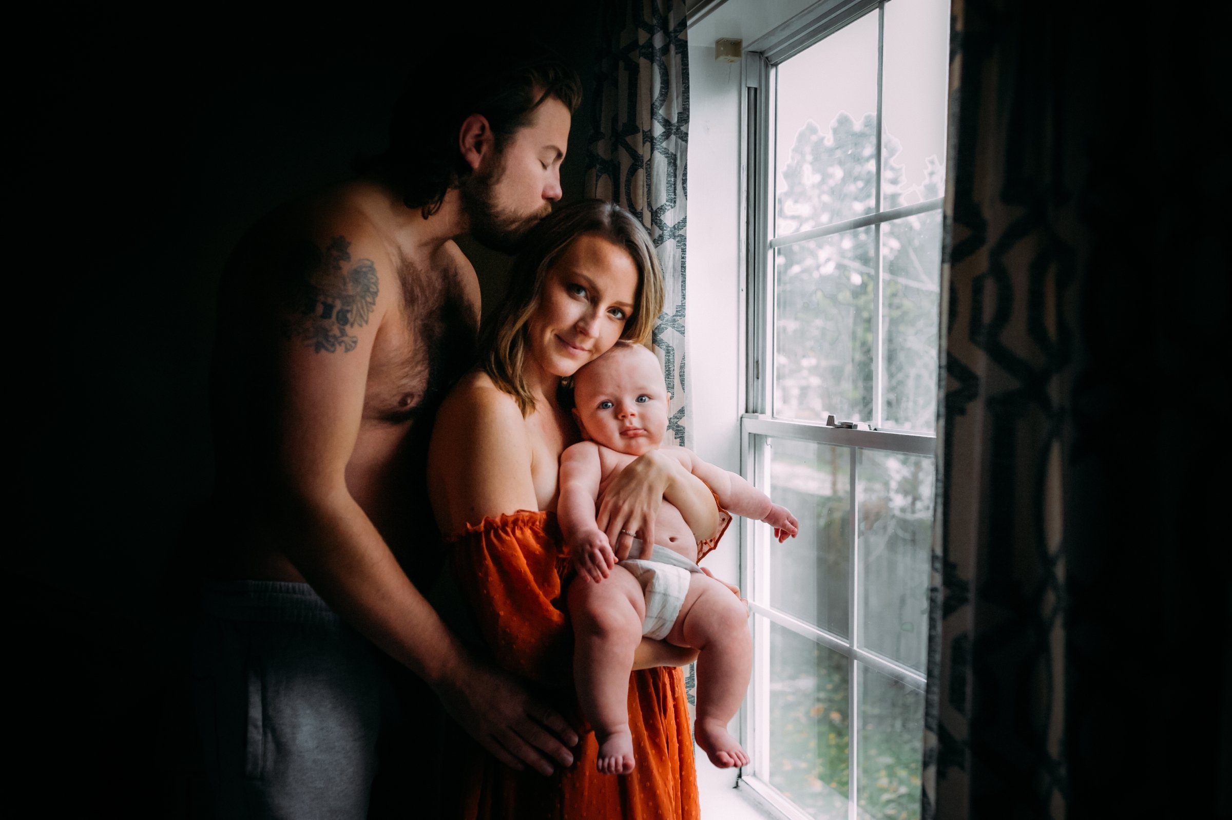 intimate family embraces by window with their baby