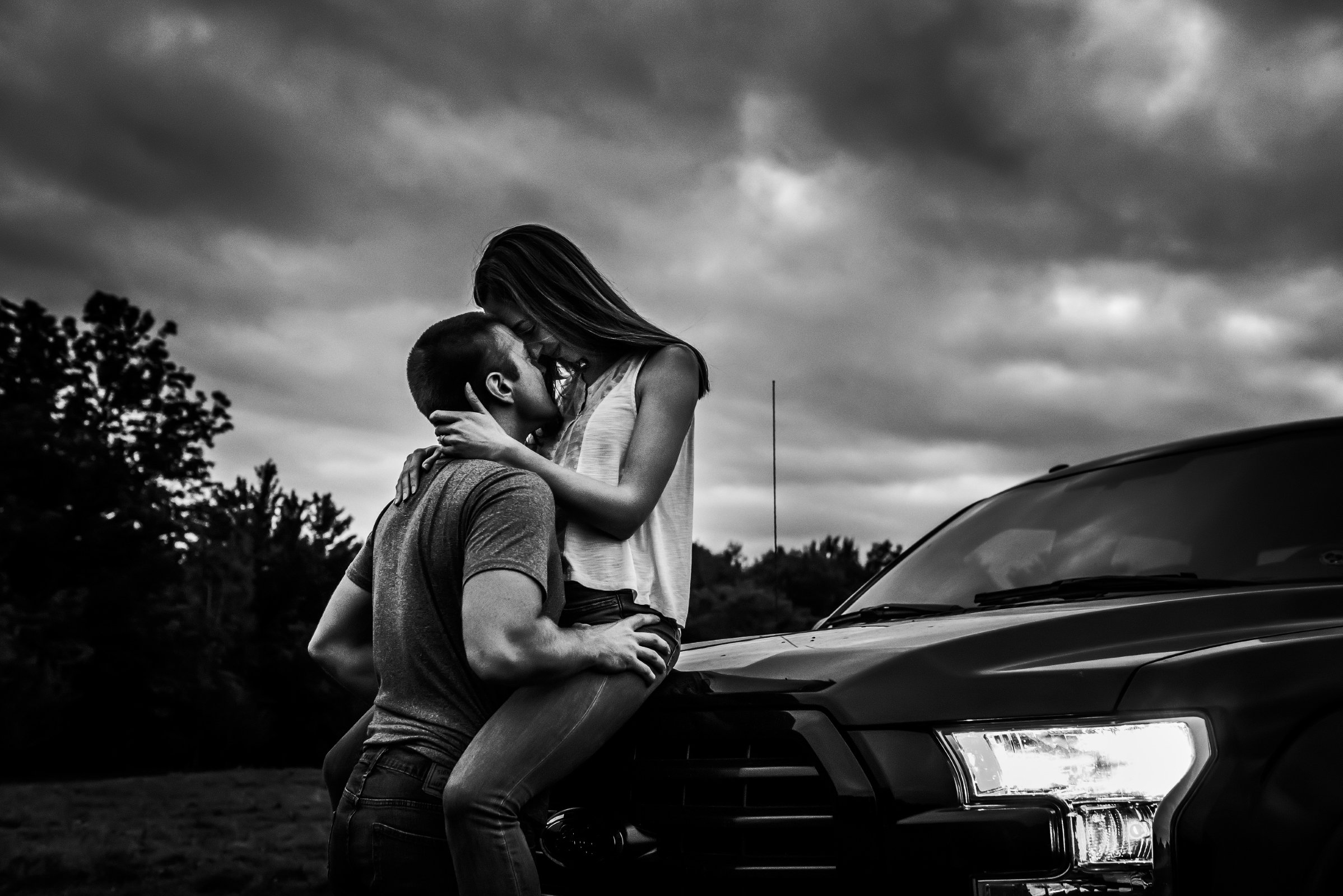 couple kisses on truck after dark for engagement photos