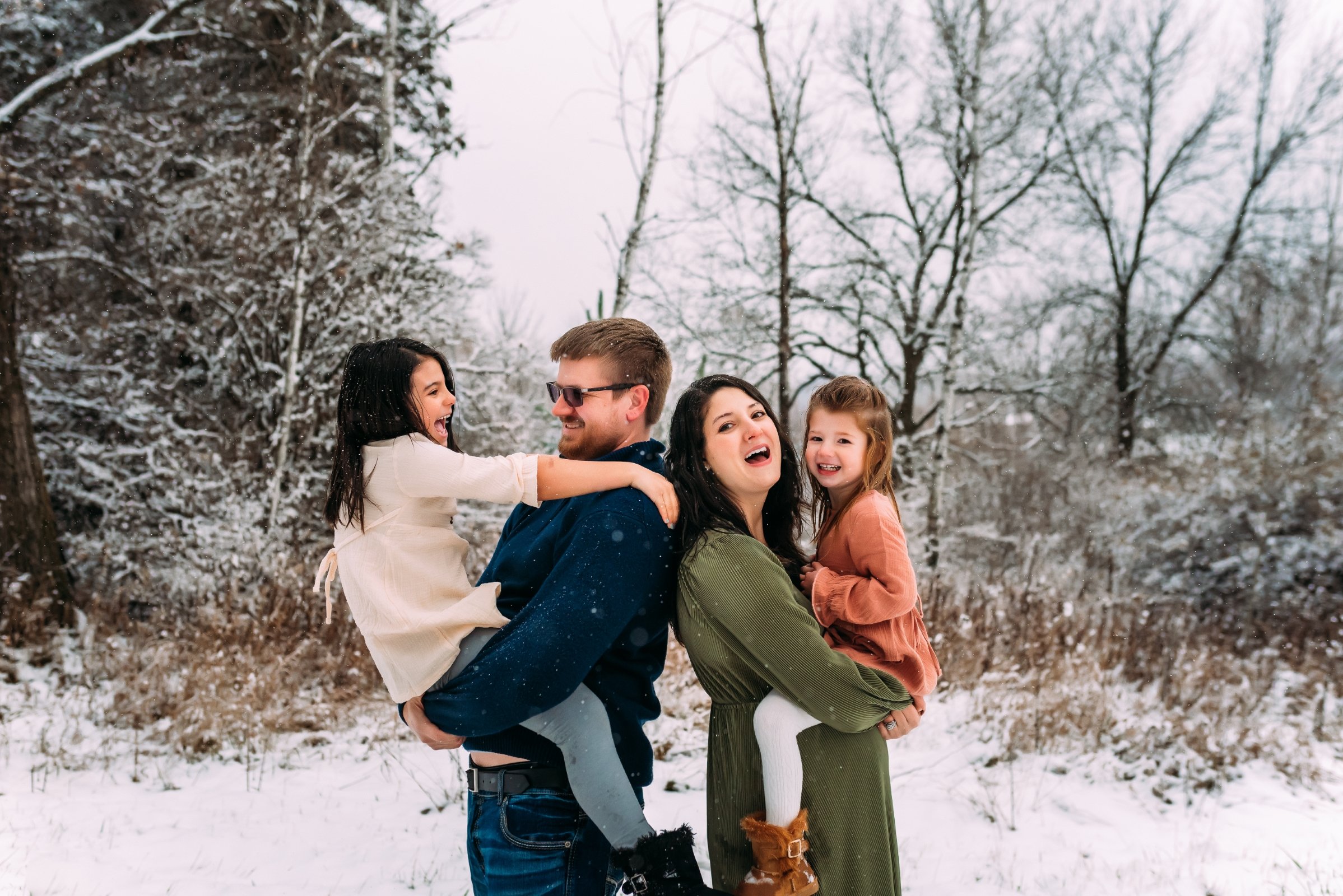 family laughs together in snow for their family photos
