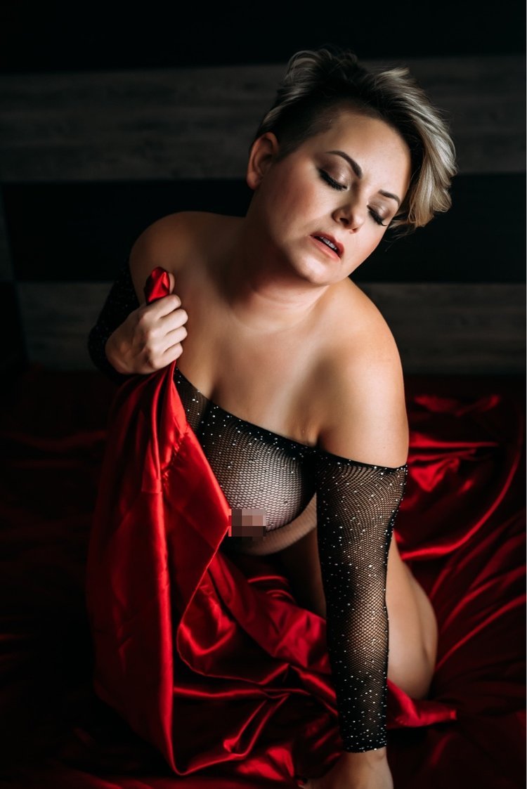women poses with red silk sheets for her boudoir session