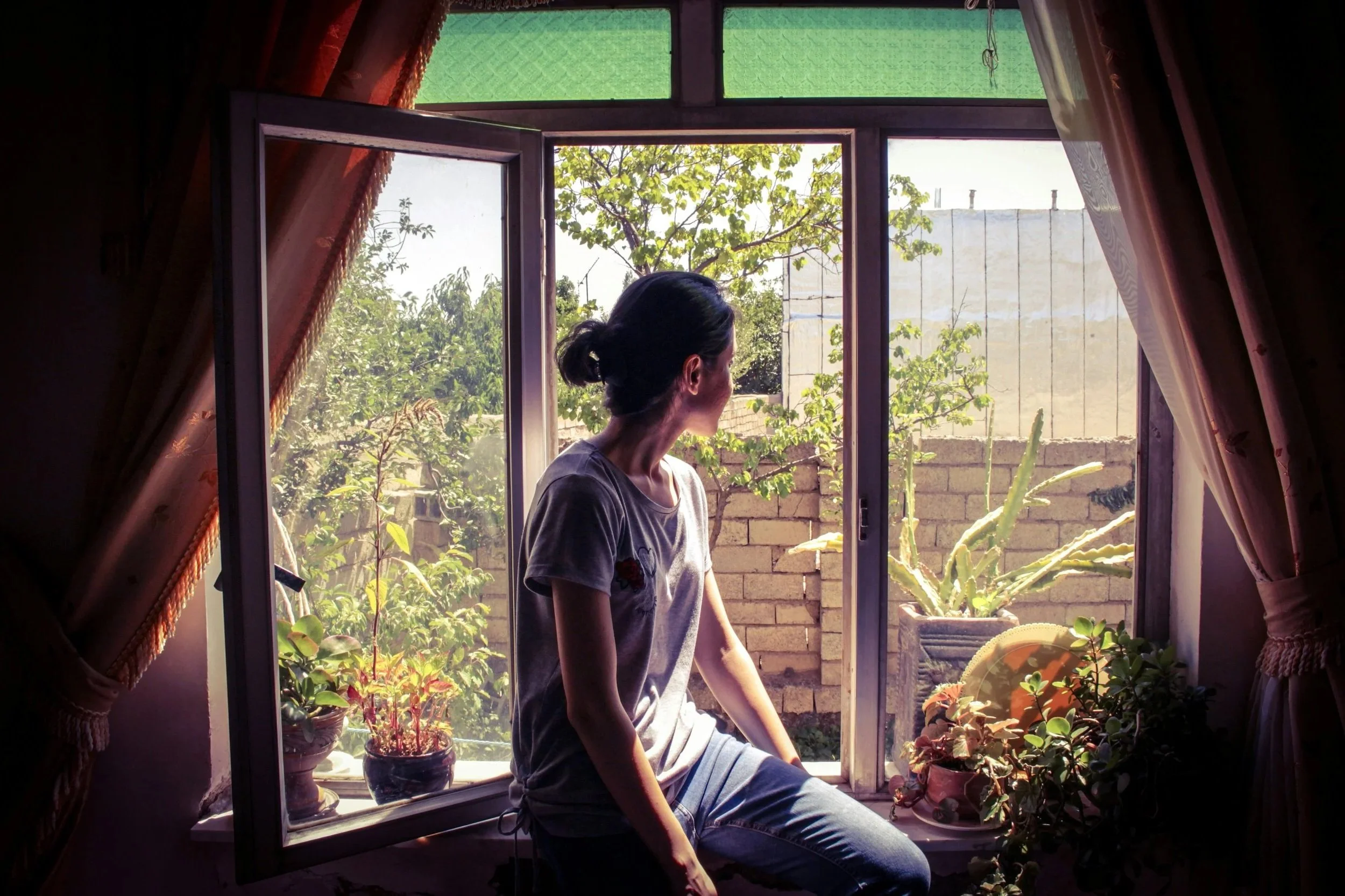 Person looking thoughtfully out a window, reflecting before beginning therapy.