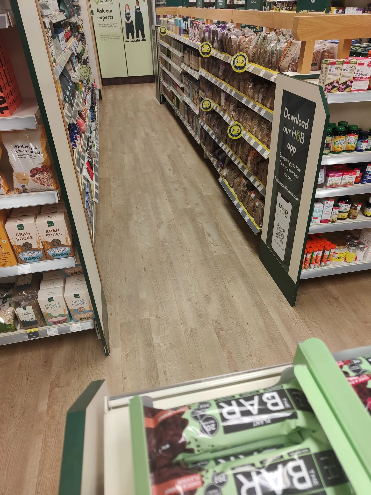 The image captures a health food retail store interior with luxury vinyl tile flooring in a light wood finish. The composition features a diagonal perspective, showcasing an aisle leading into the background. 