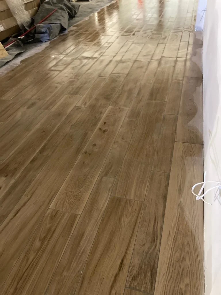 A close-up of a wooden floor composed of light brown planks arranged in a linear pattern. The image captures the grain texture of the wood, with subtle variations in colour.