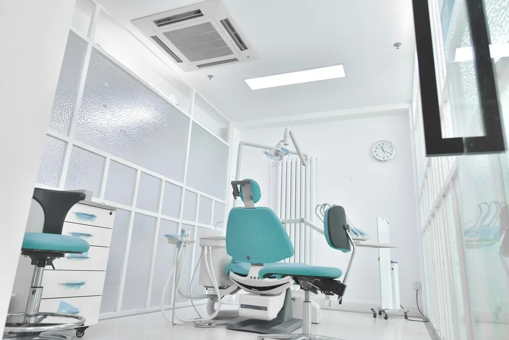 Dental examination room with dental chair, stool, and equipment in a bright, clean space.