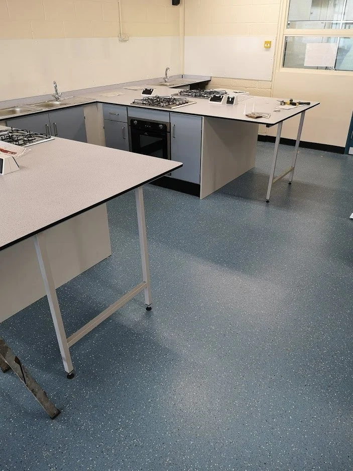 An empty commercial kitchen with a countertop, a stove with four burners, sinks, and cabinets.