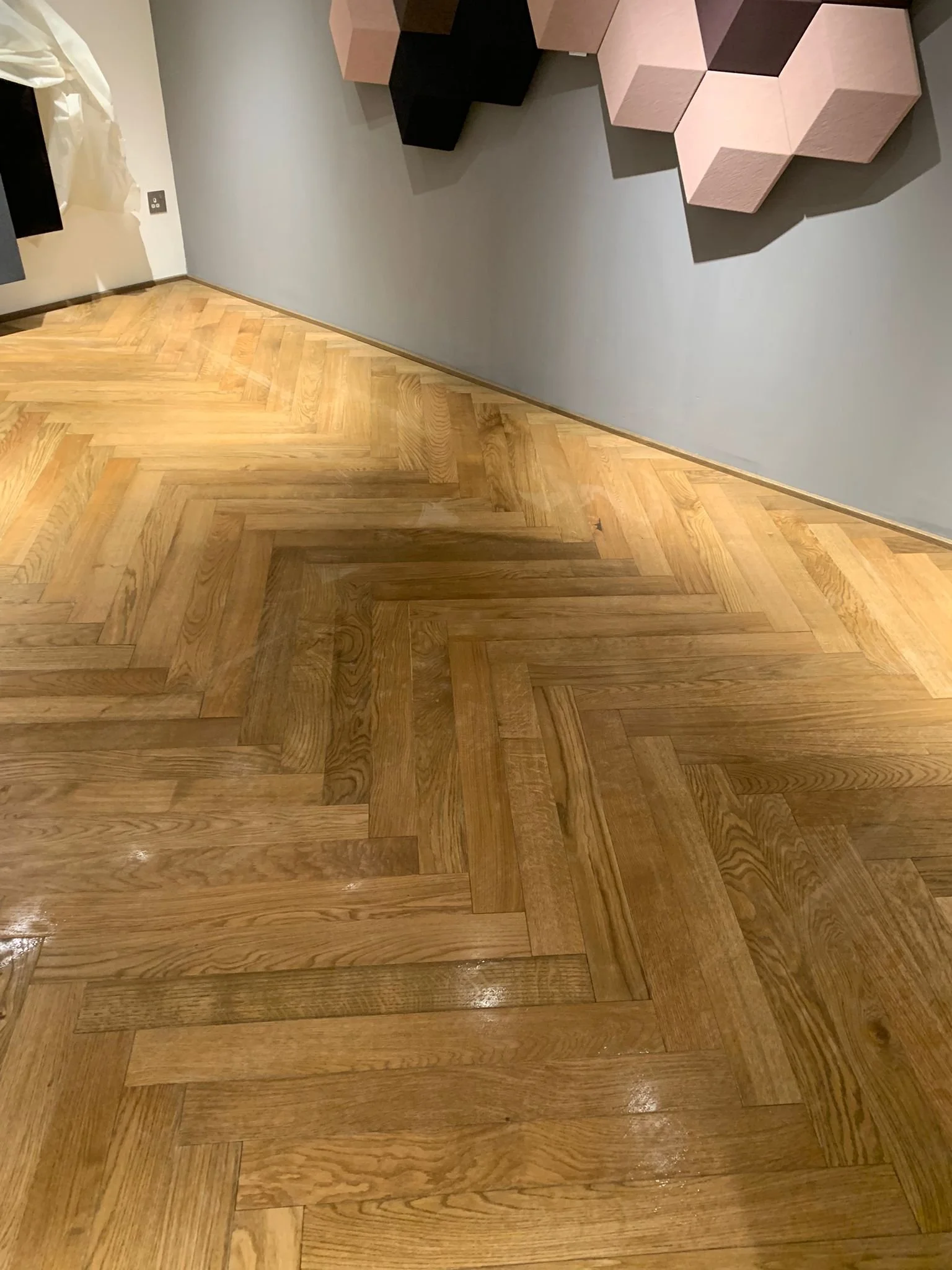 A close-up view of a herringbone pattern timber floor. The image is taken at an angle, showcasing the planks arranged in a zigzag pattern.