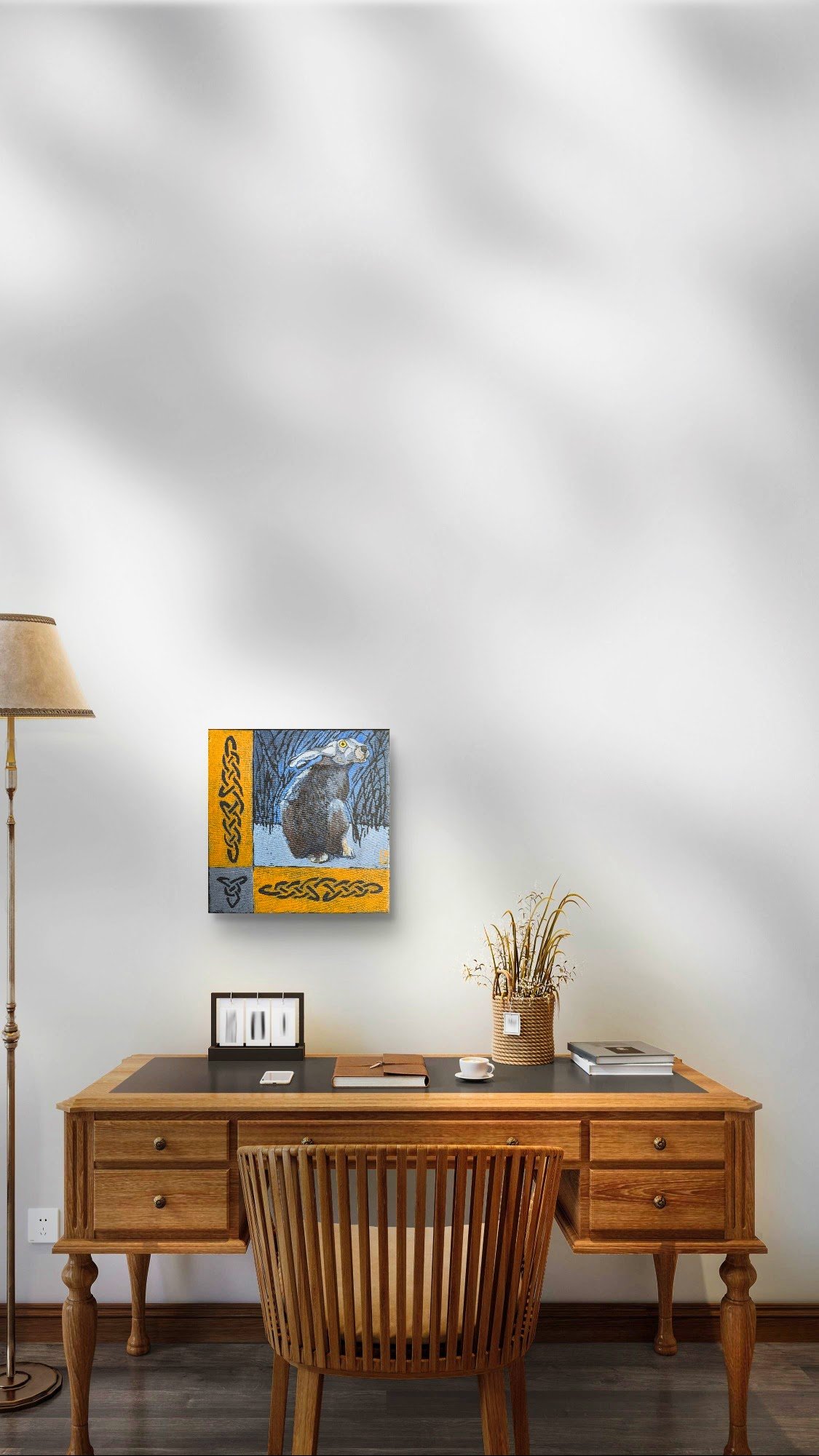 Home office with wooden desk, chair, lamp, artwork on white wall, and decorative plant. On the wall is a hare painting.