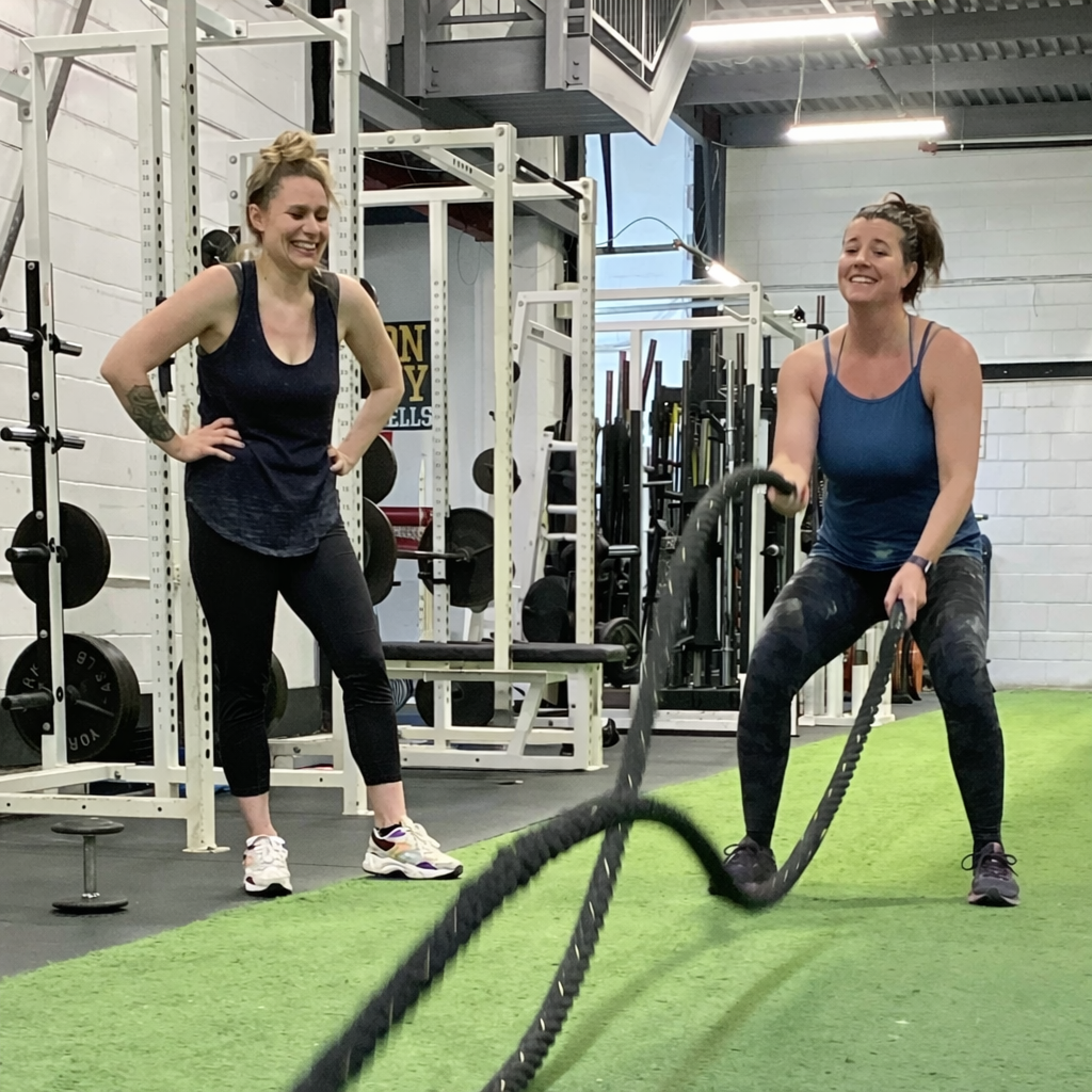 Partner fitness. Two women work out with battle ropes.
