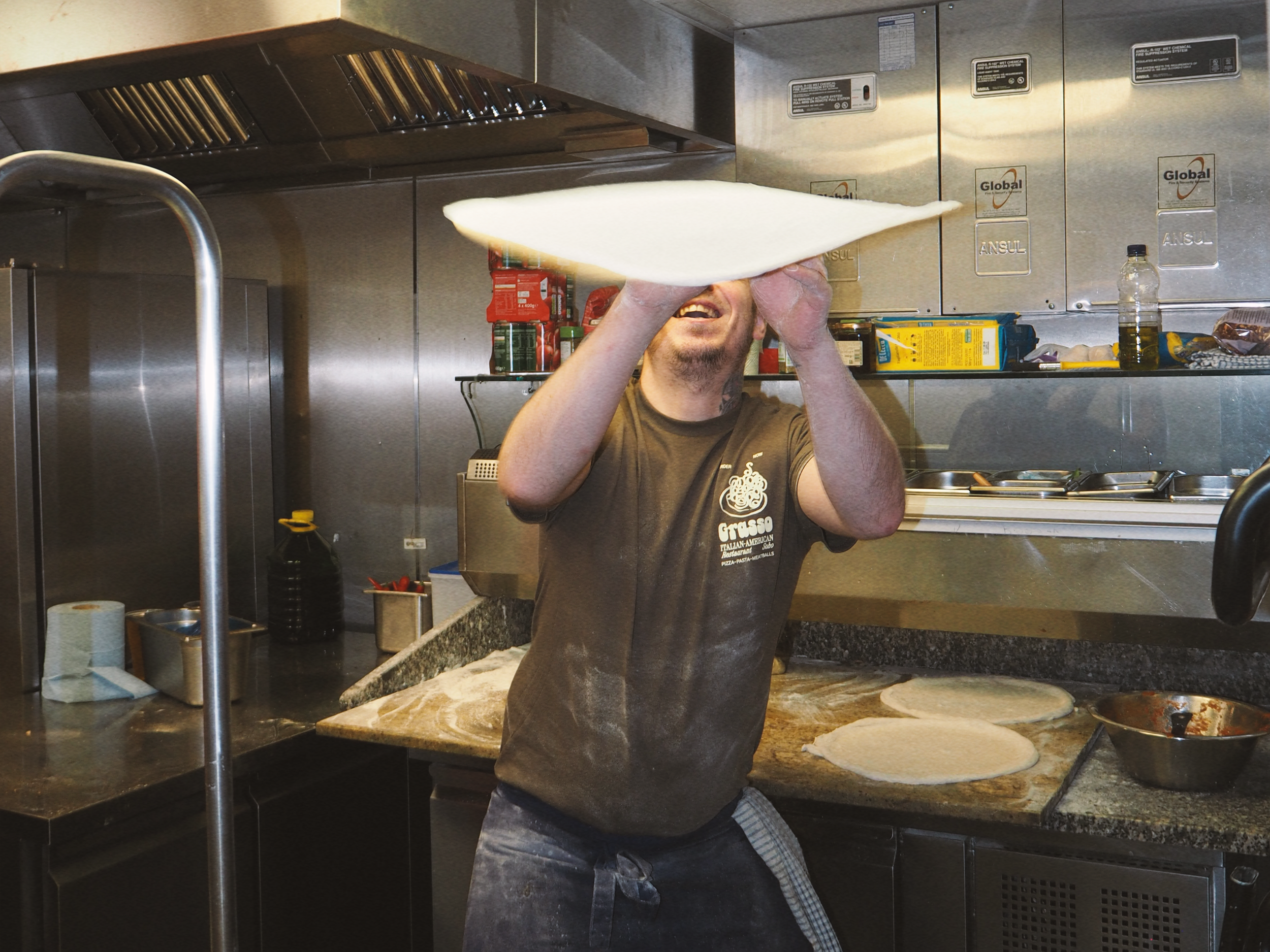 Man tossing pizza dough in a kitchen