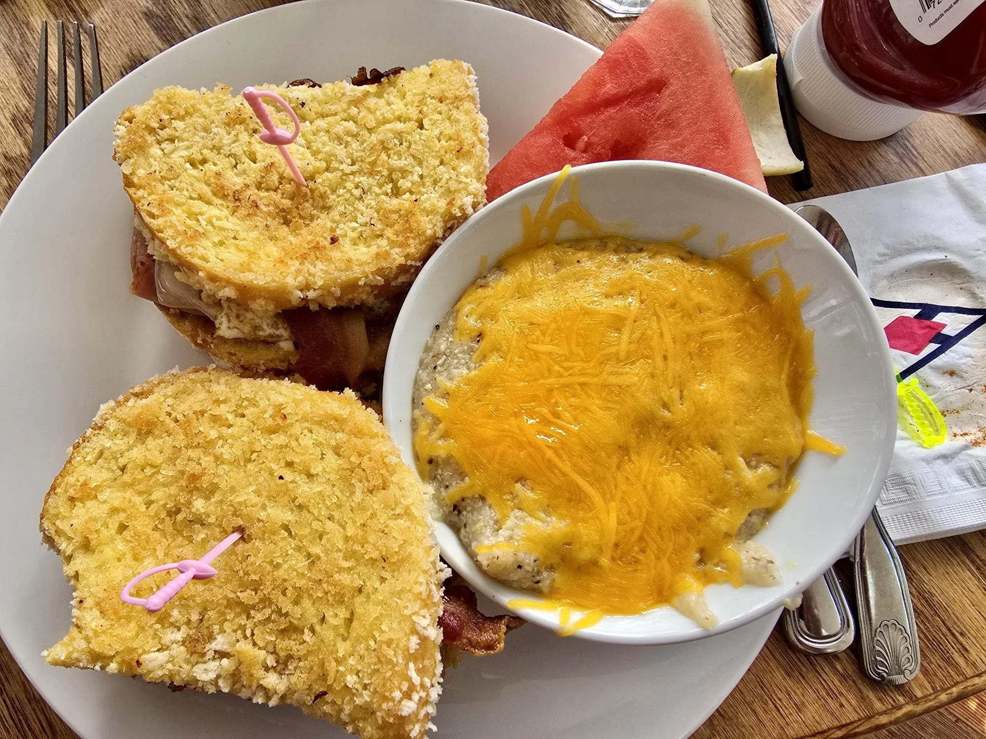 Plate with two slices of cake, a bowl of cheesy baked eggs, a slice of watermelon, and a slice of cantaloupe on a wooden table.