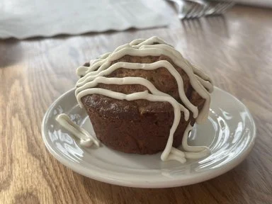 Chocolate muffin topped with white icing on a white plate.