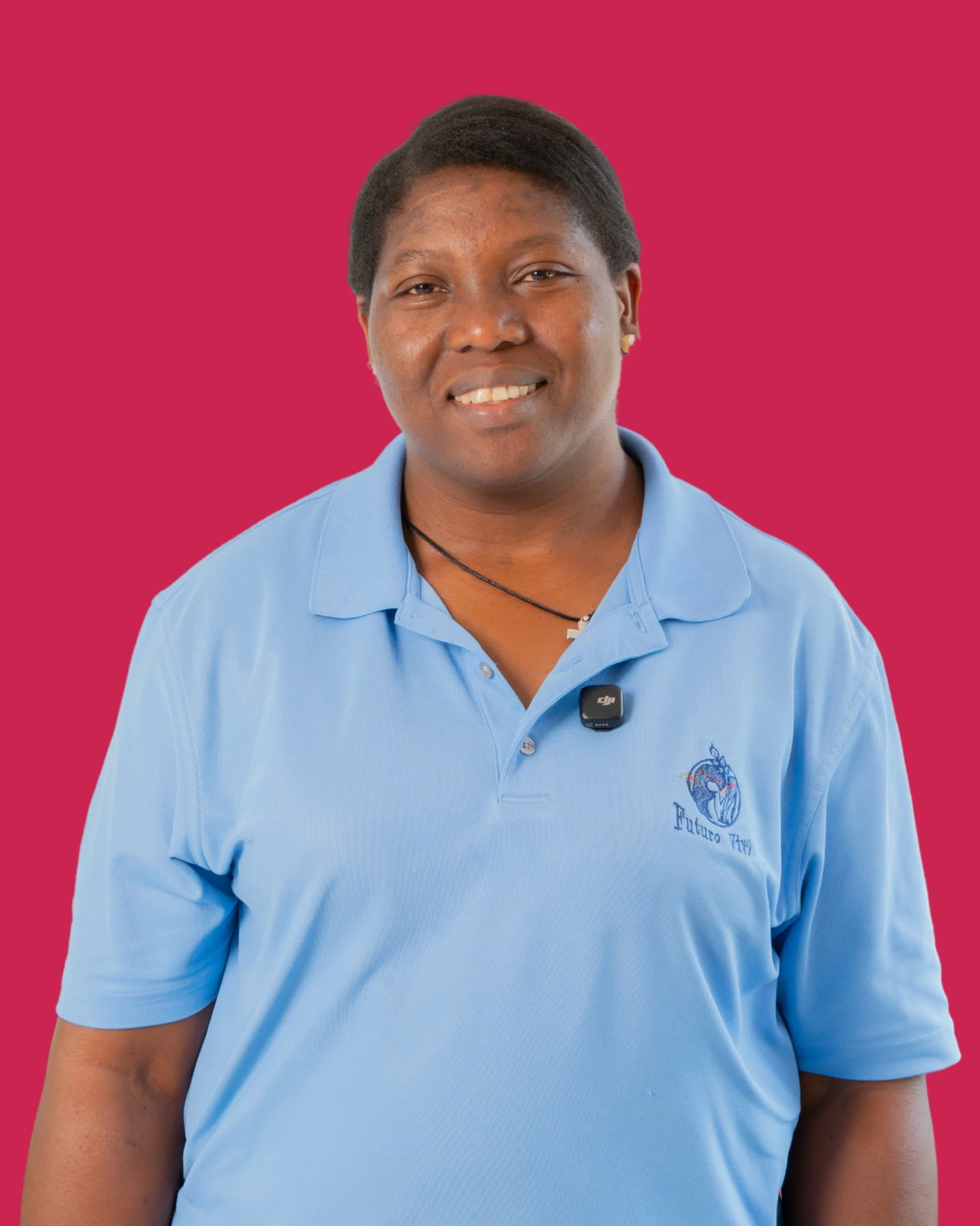 Un hombre con piel oscura, cabello corto y peinado hacia un lado, con camiseta azul claro y fondo rosa. Varias camisetas con logotipos y textos, y un pequeño micrófono en el pecho.