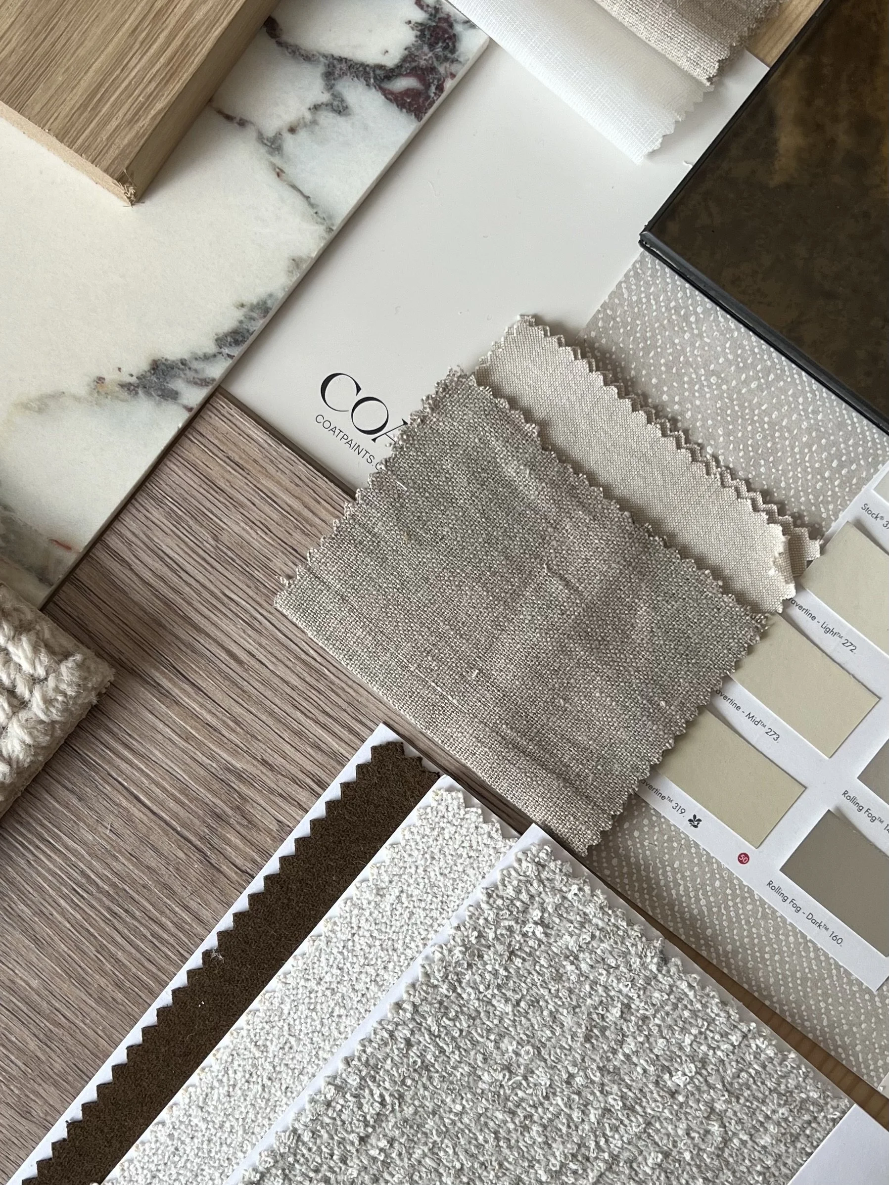 A collection of interior design materials including fabric swatches, tiles, and paint chips in neutral tones and various textures, arranged in a flat lay.