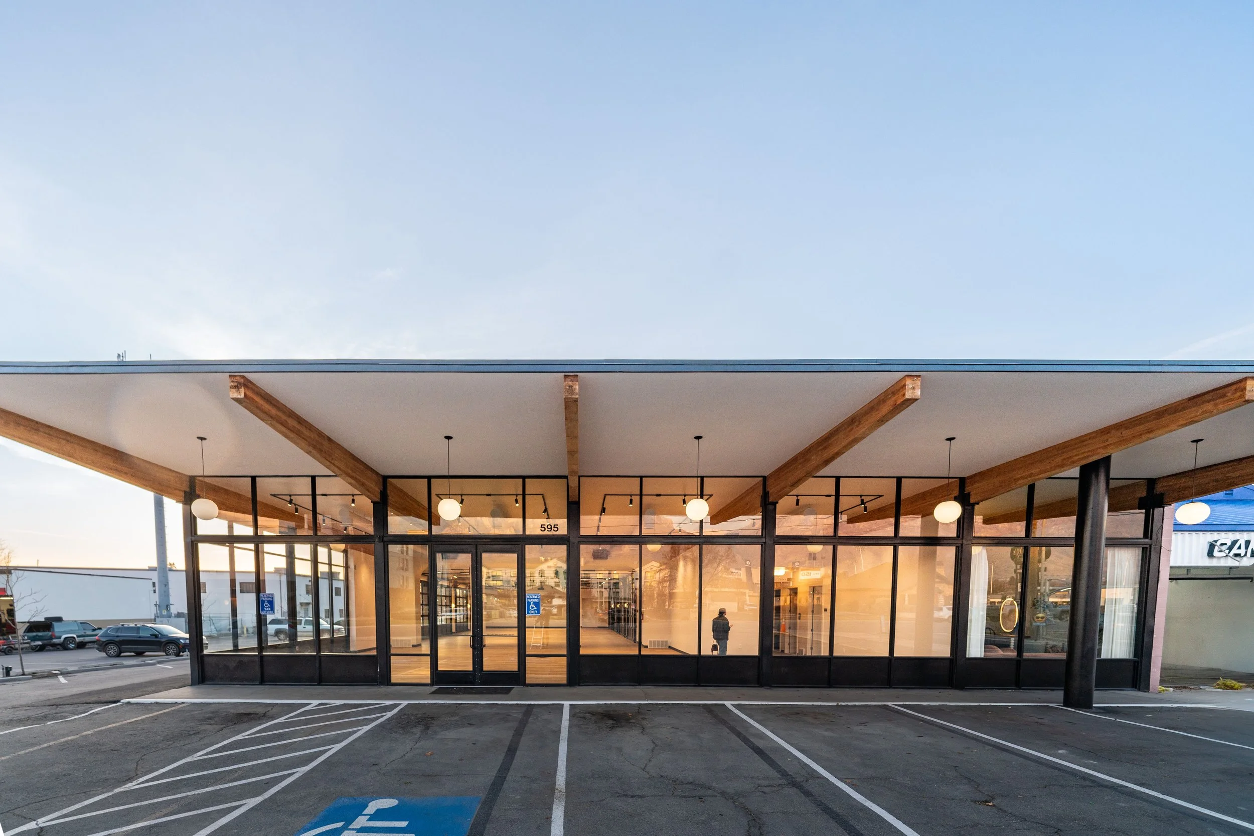 Modern commercial building with glass front, parking lot in front, and visible handicap parking space.